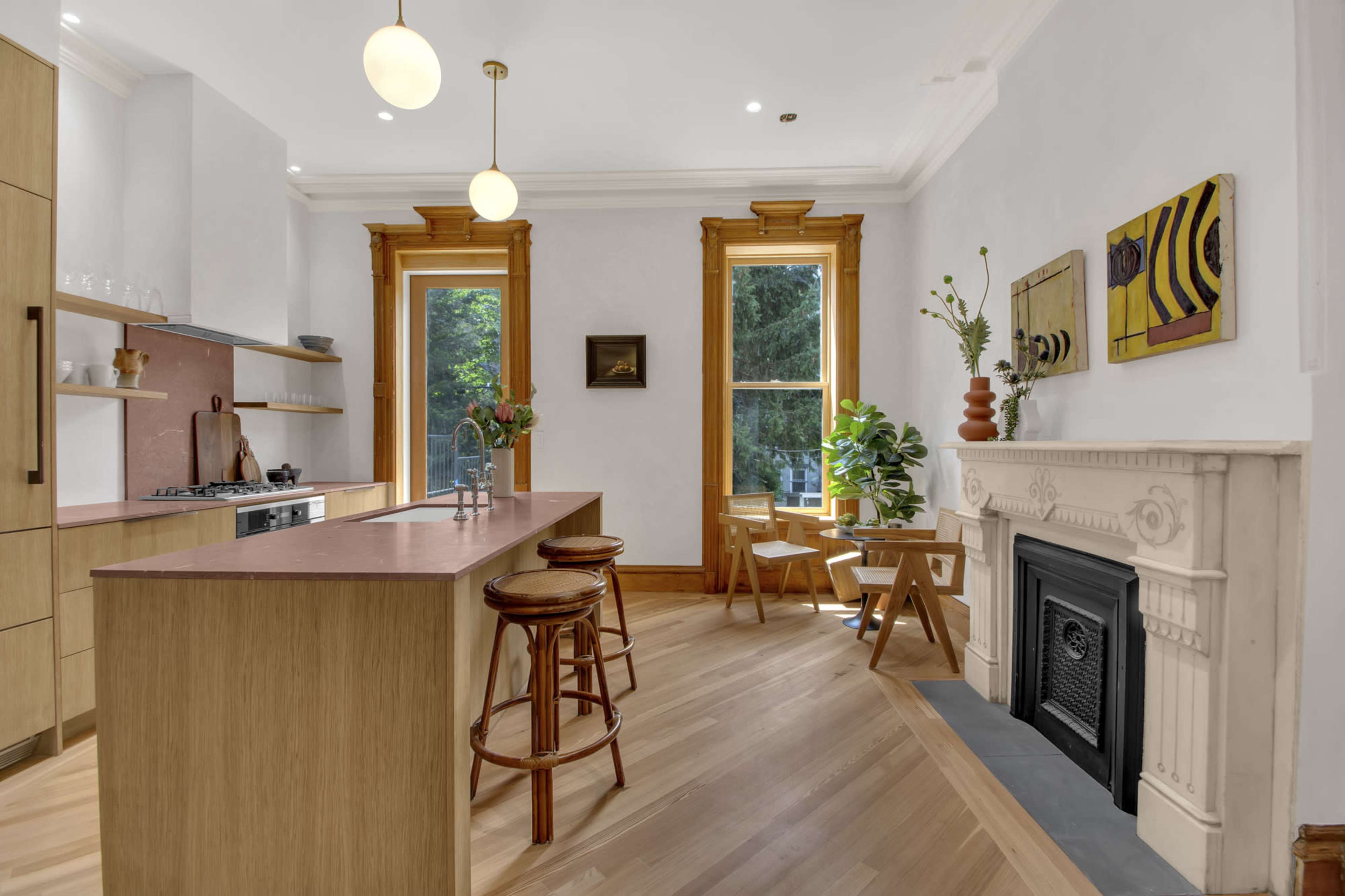 The image shows a modern kitchen featuring a central island with bar stools, a gas stove, and large windows with natural light illuminating the space.