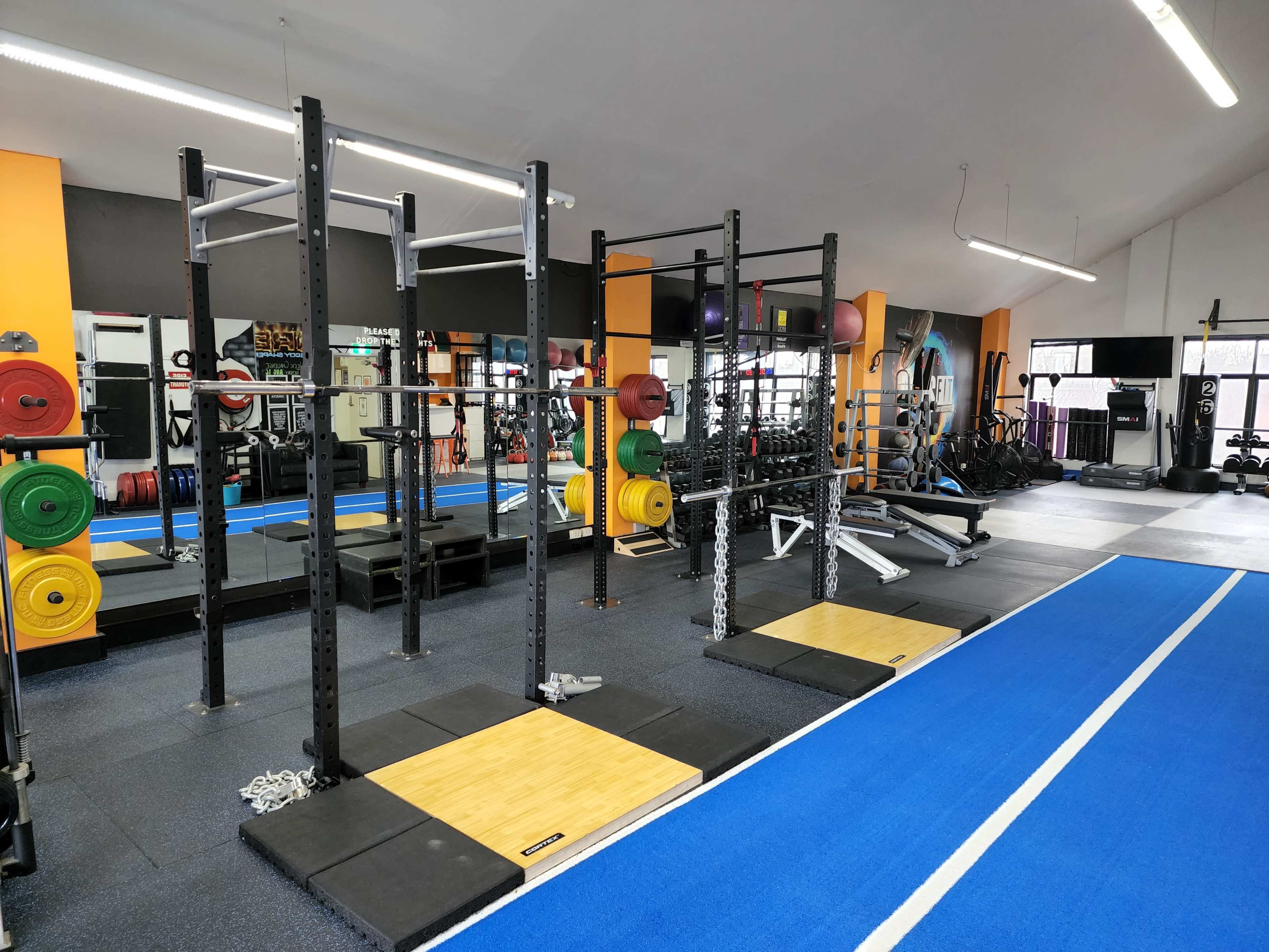 A gym interior with weightlifting equipment, including a squat rack and barbells, set on a blue rubber floor.