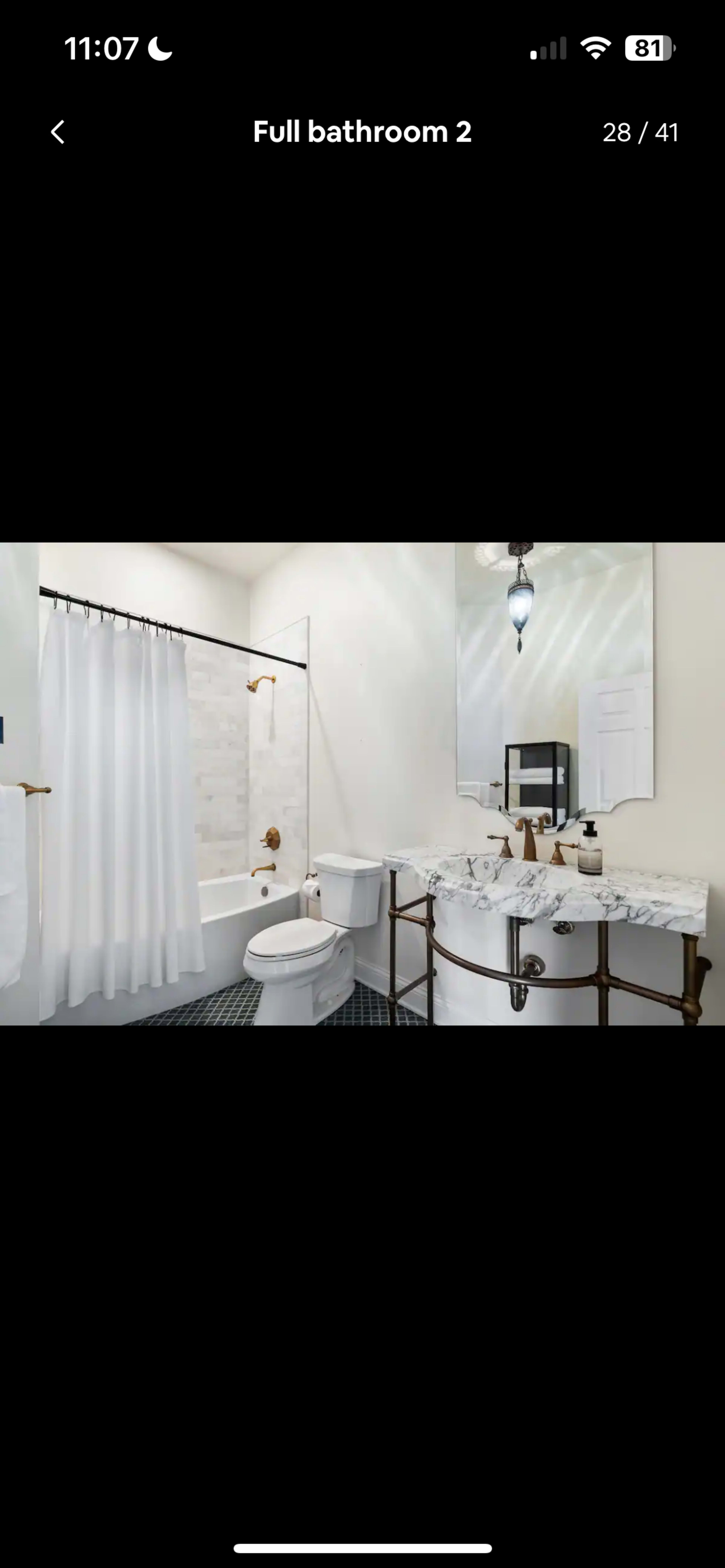 The image shows a full bathroom featuring a clawfoot bathtub, a toilet, a sink with a marble countertop, and a shower area with a glass door.
