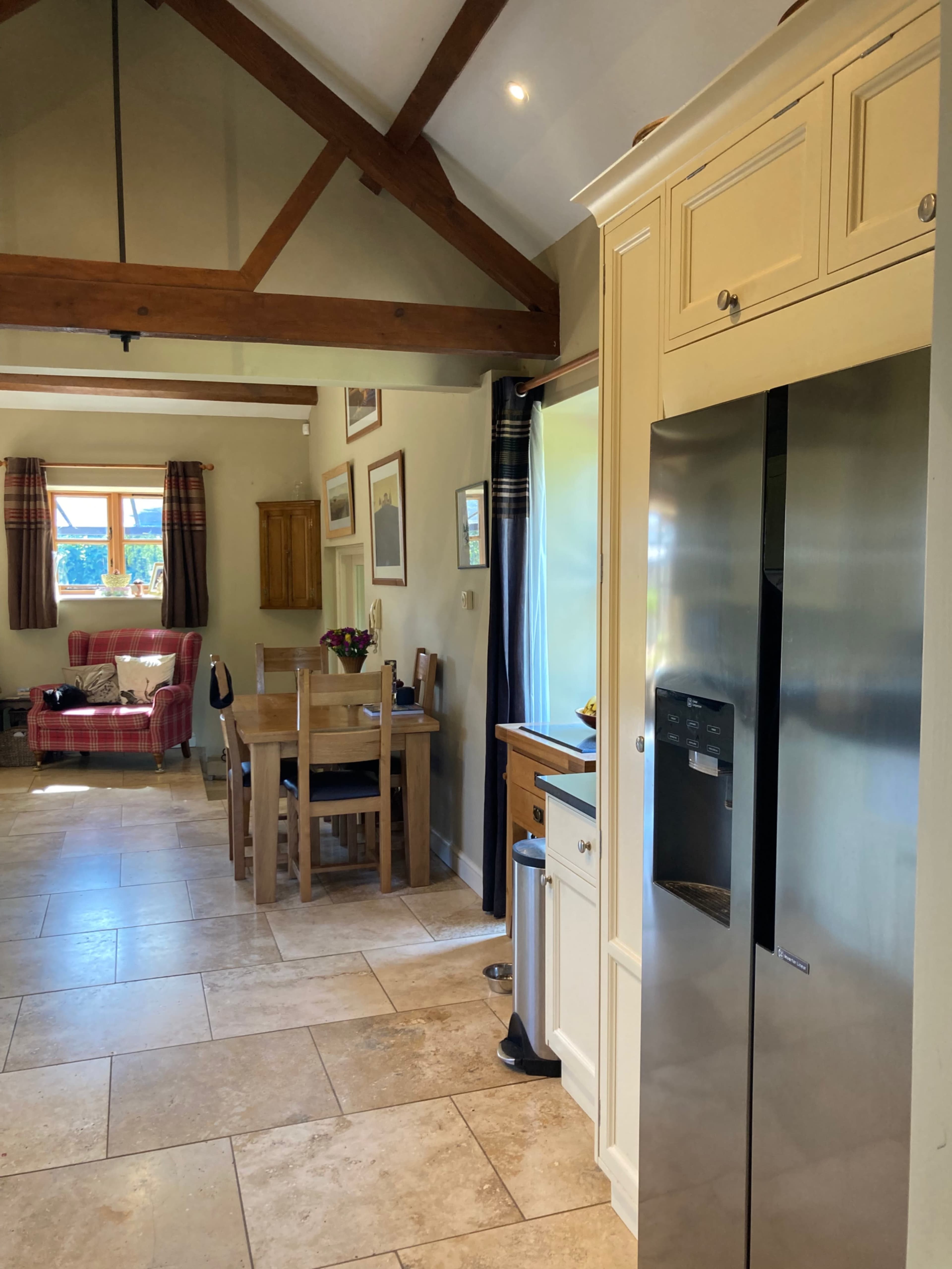 A kitchen with stone tile flooring features a stainless steel refrigerator, wooden dining table, and a cozy seating area in the corner.