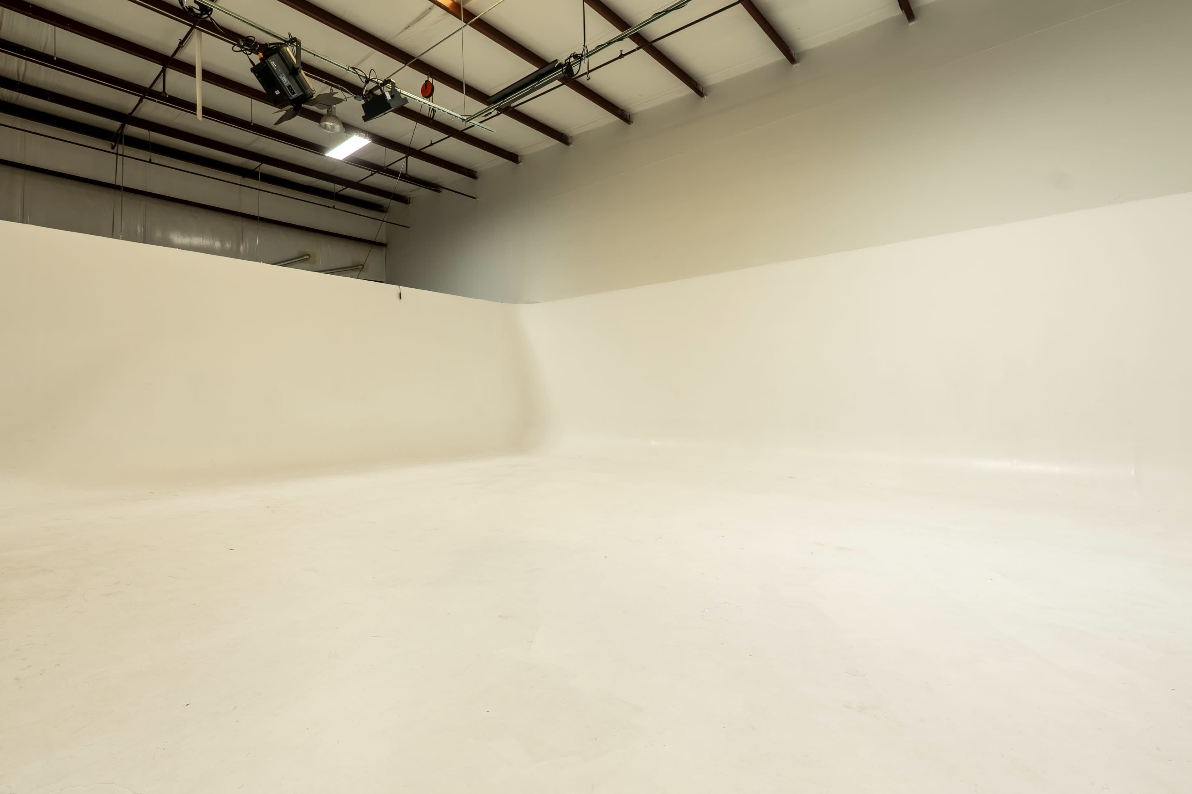 The image shows a spacious, empty studio with a seamless white backdrop and high ceilings.