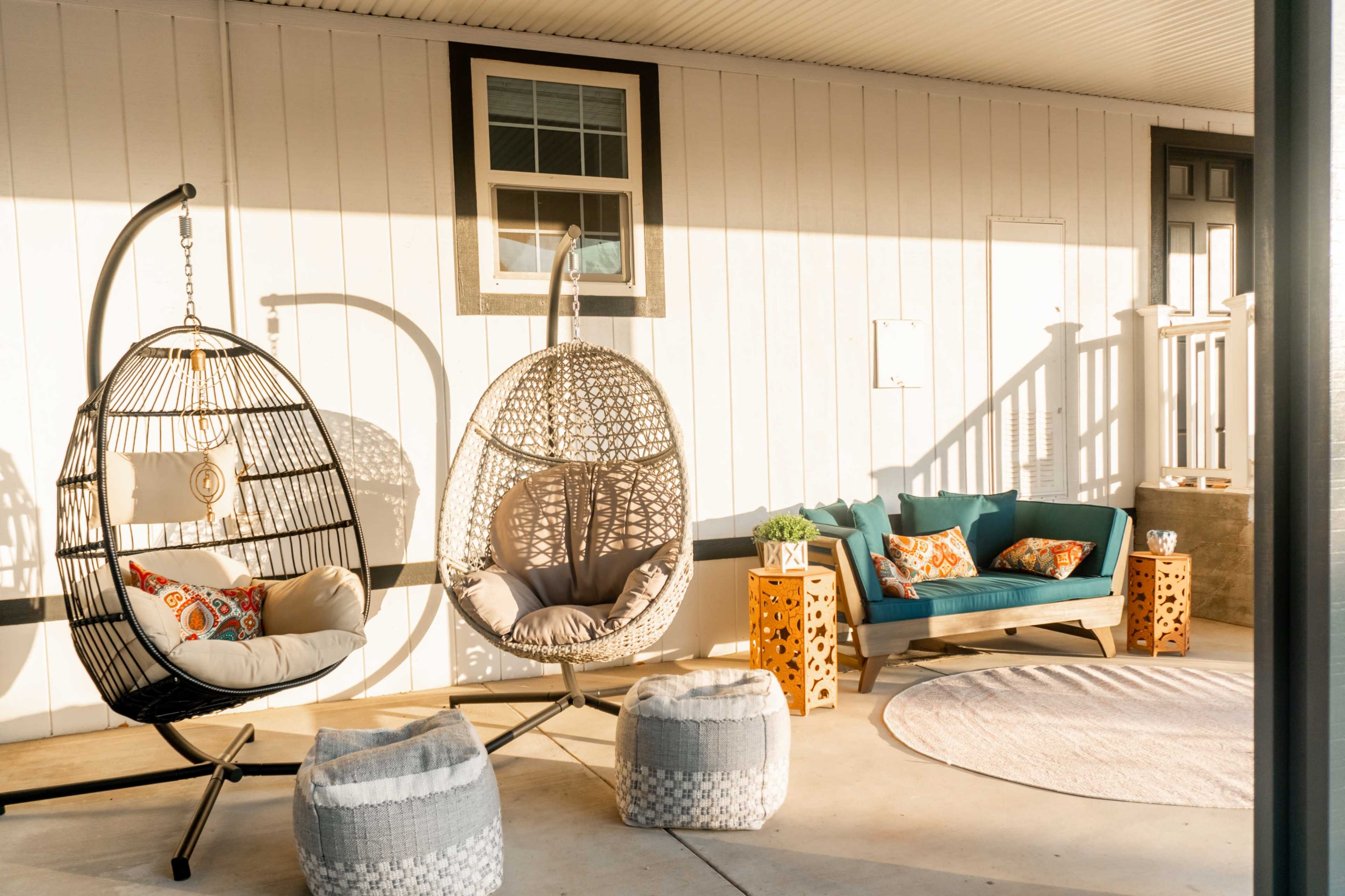 A stylish porch area with two hanging chairs, a teal couch, and decorative pillows, accompanied by light-colored poufs and a round rug.