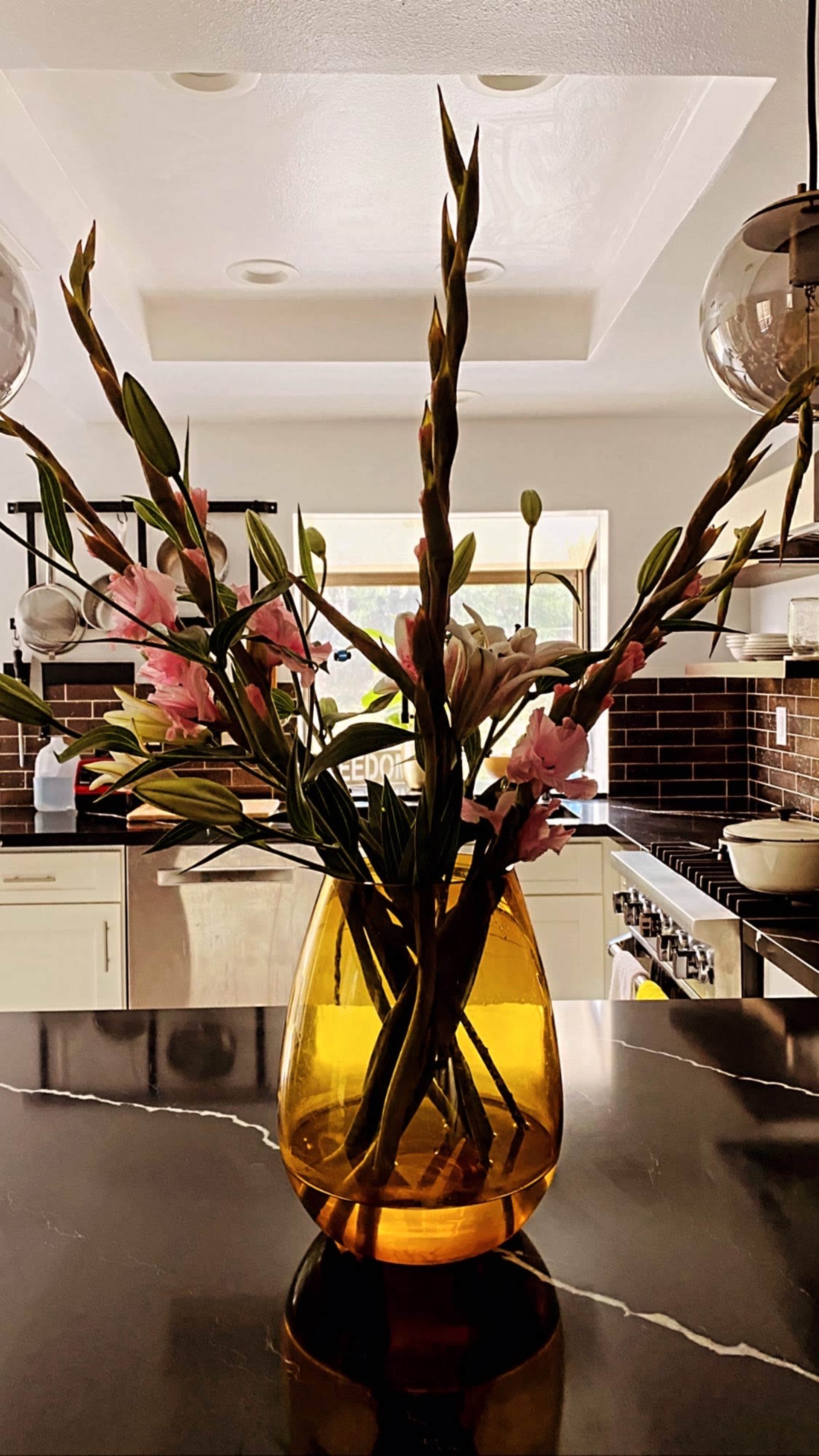 A glass vase filled with flower stems sits on a dark marble kitchen countertop.