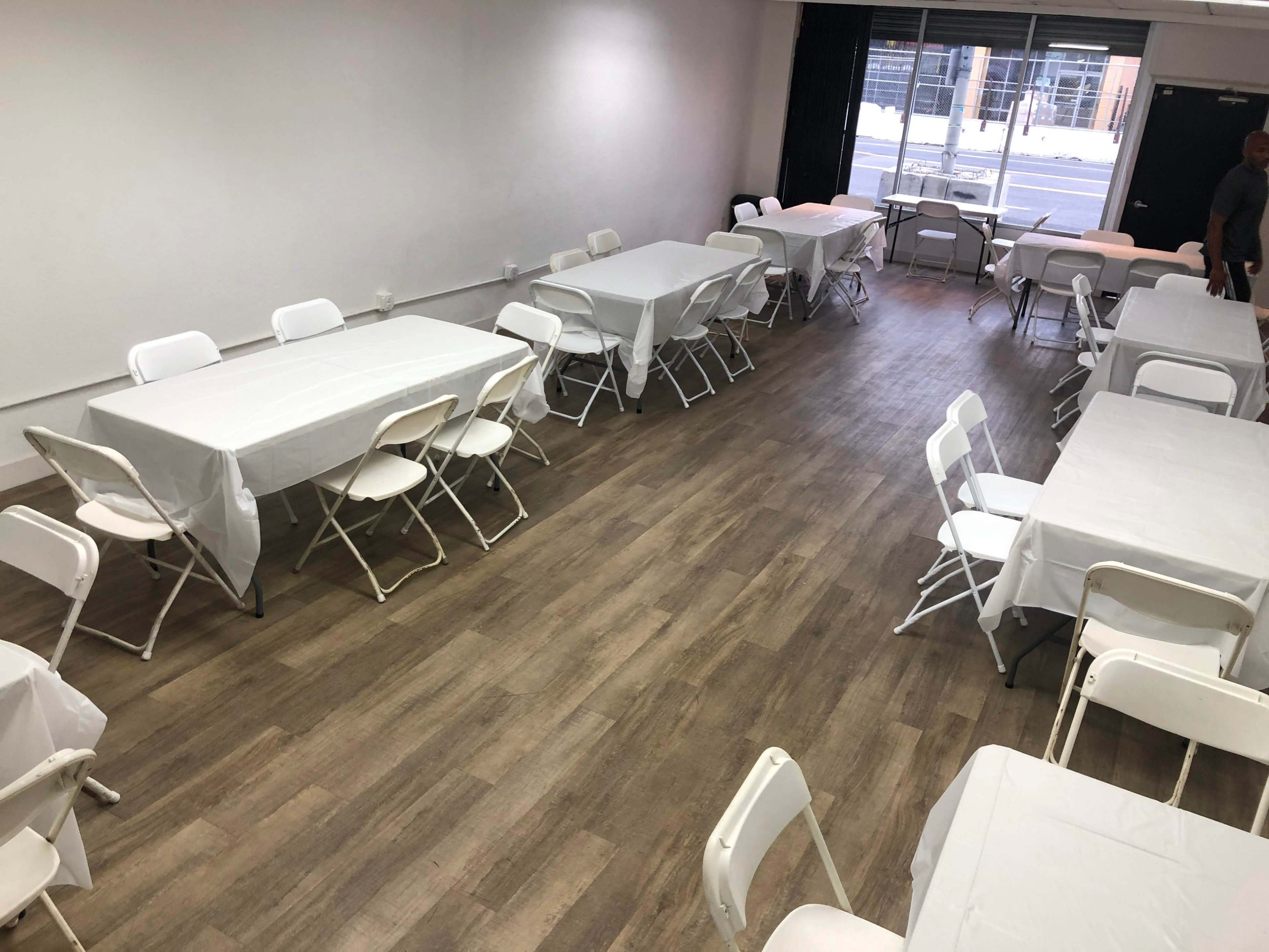 A spacious room with multiple tables covered in white tablecloths and arranged with folding chairs.