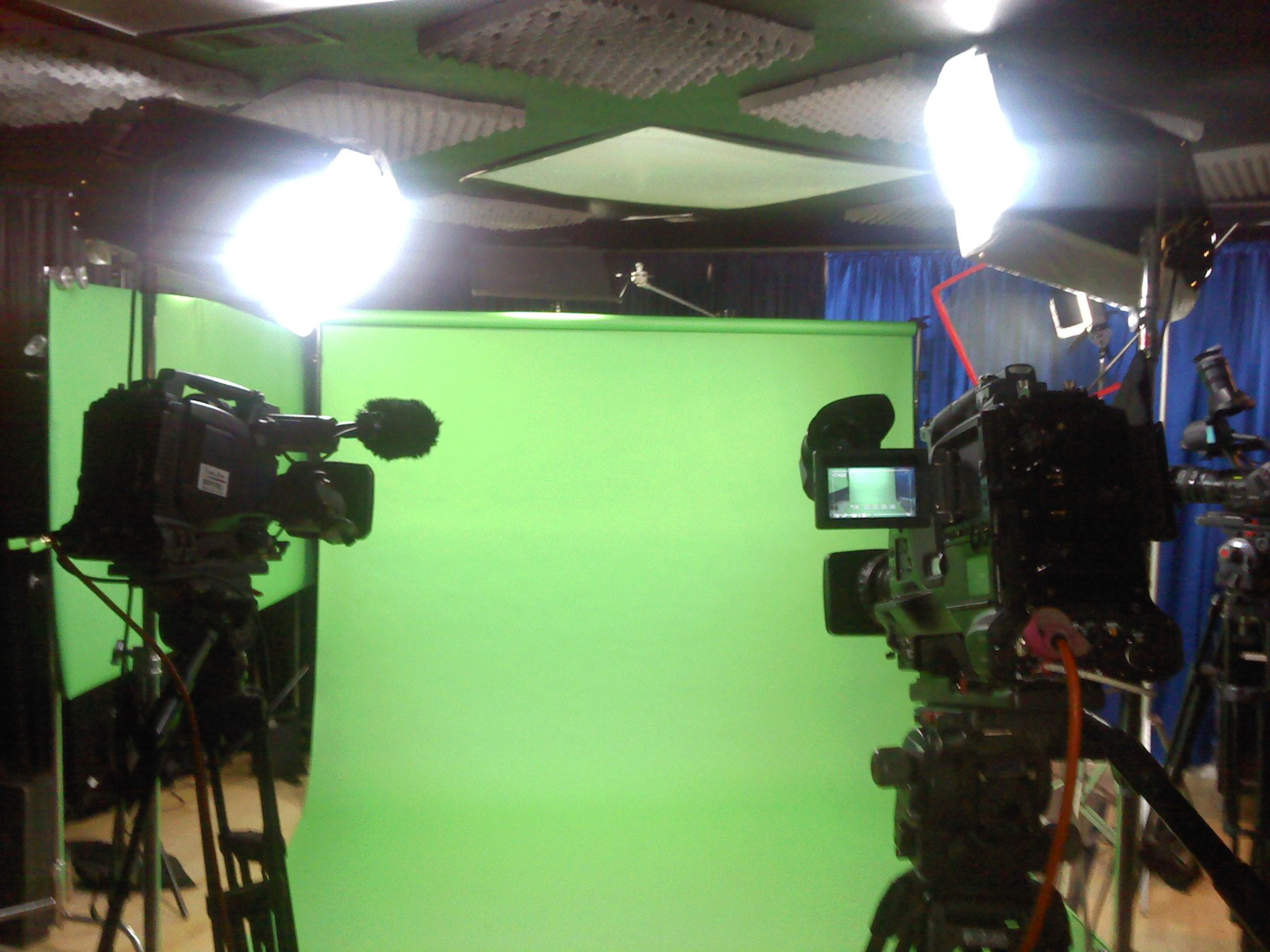 Two video cameras positioned in front of a green screen, with studio lighting set up around them.