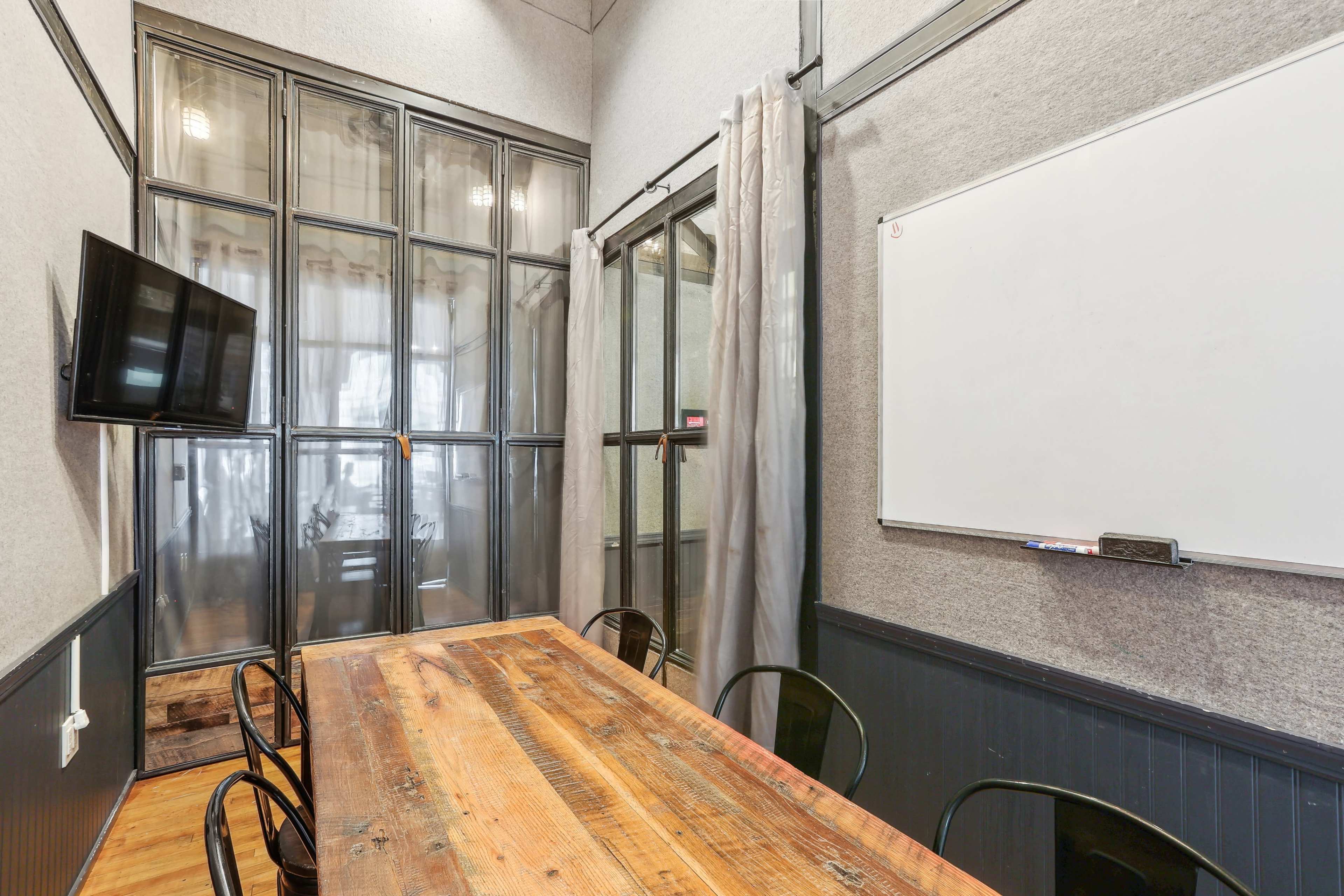 The image shows a conference room with a wooden table, black chairs, a wall-mounted TV, and a whiteboard.