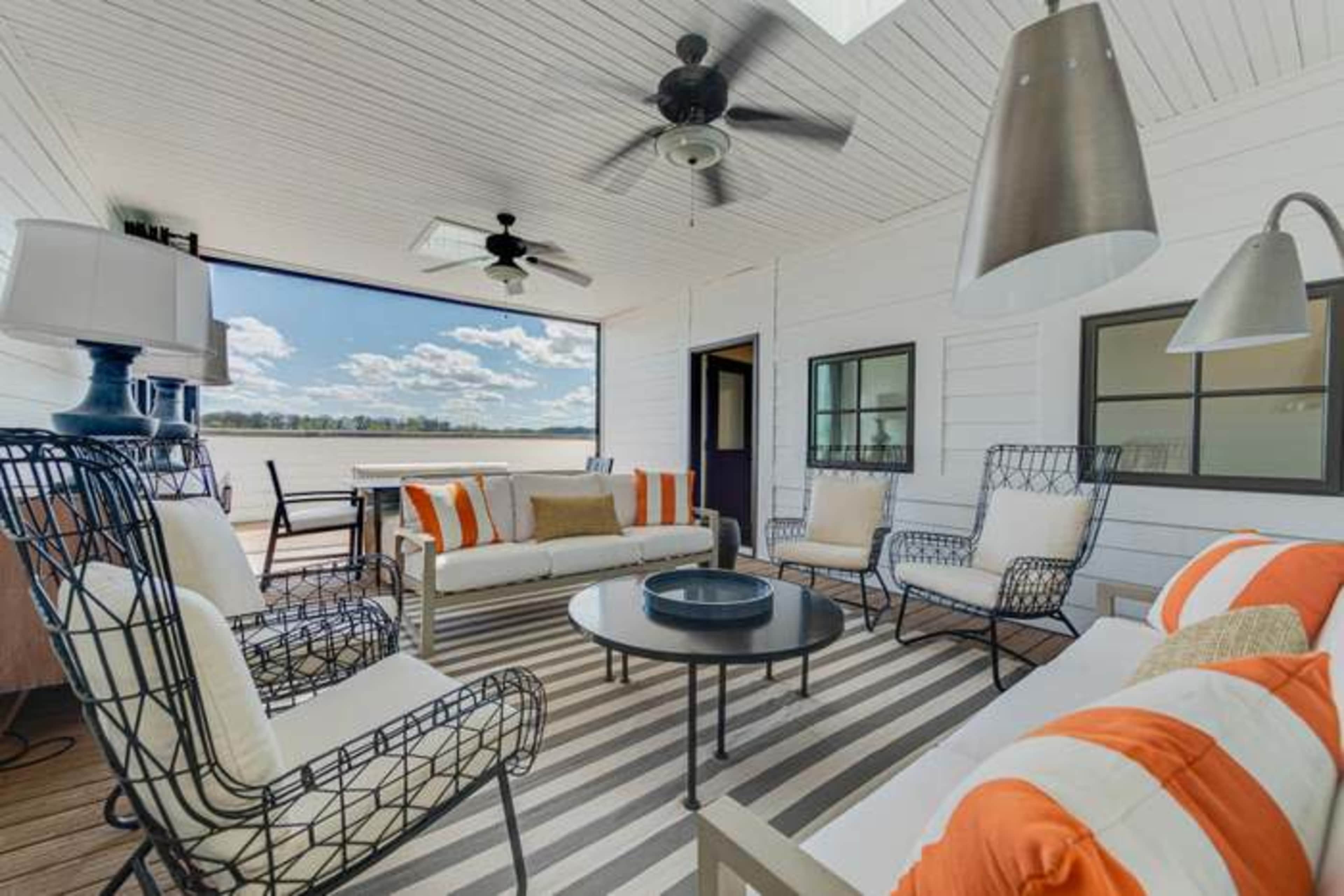 The image shows a covered outdoor seating area with metal framed chairs and sofa, a round table, and a light fixture, all arranged on a striped rug.