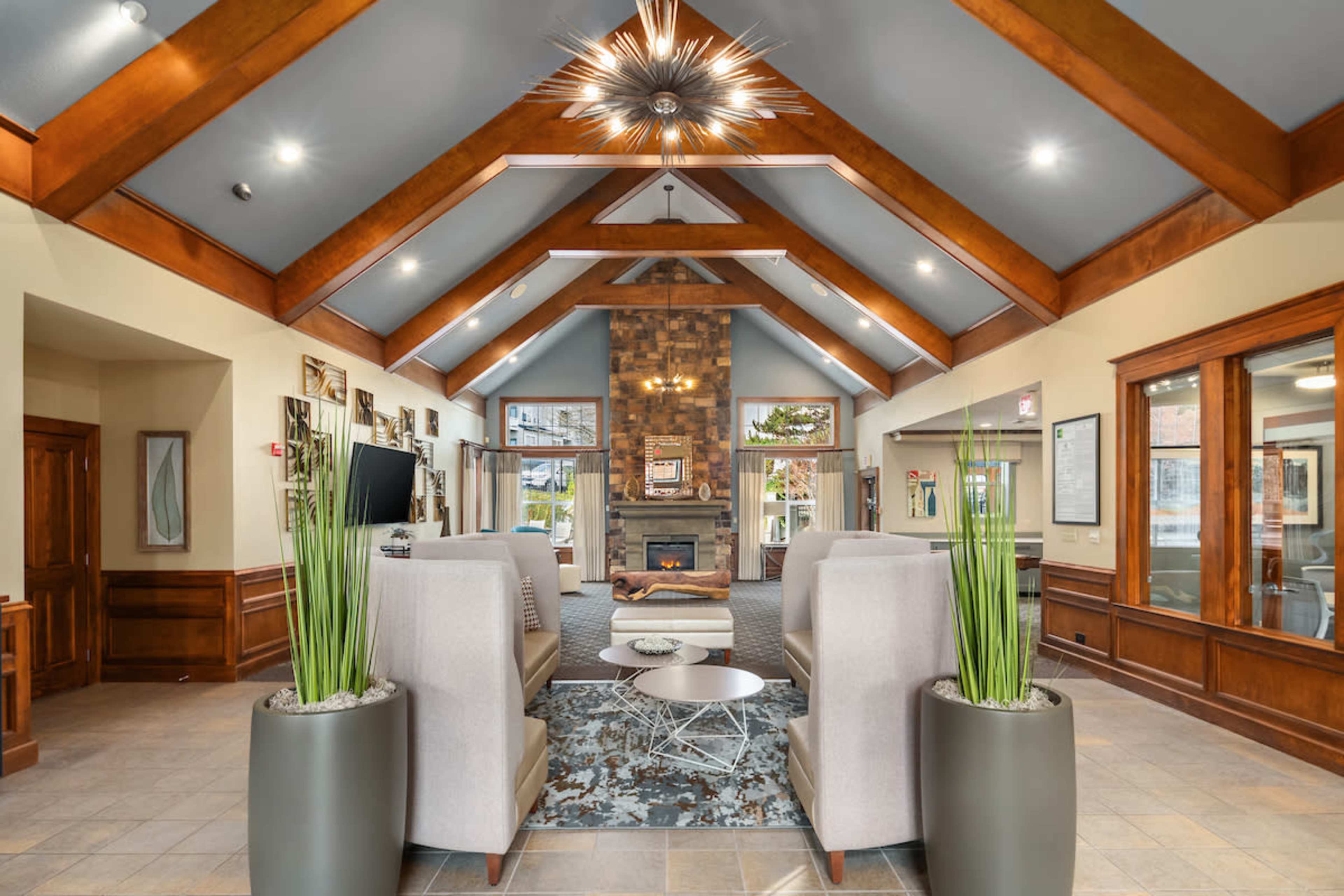 The image shows a spacious lobby with high wooden ceilings, a central stone fireplace, and contemporary seating arrangements on either side.