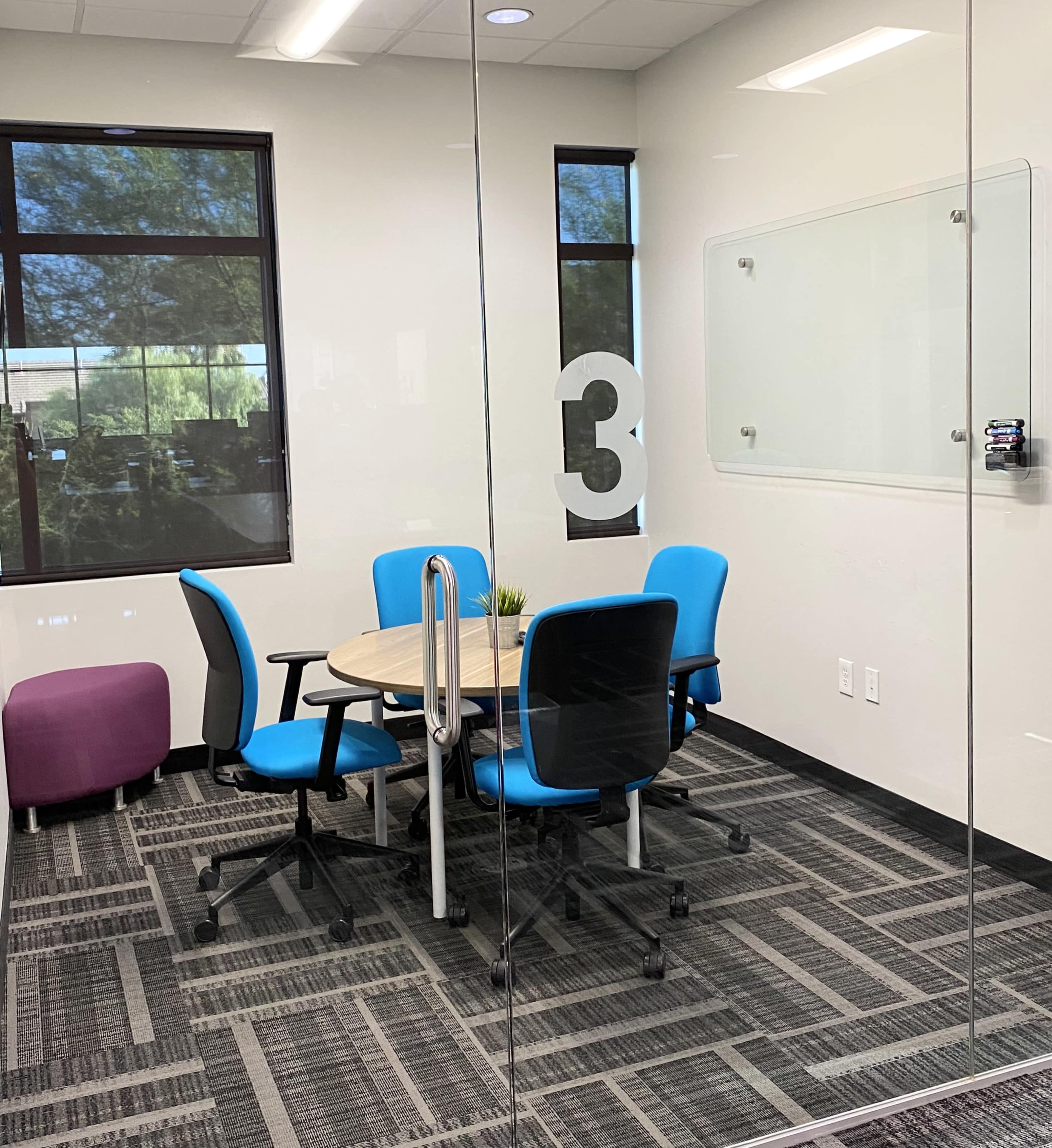 A conference room with a round table and four blue chairs is visible through a glass wall, featuring a large number "3" on the door.