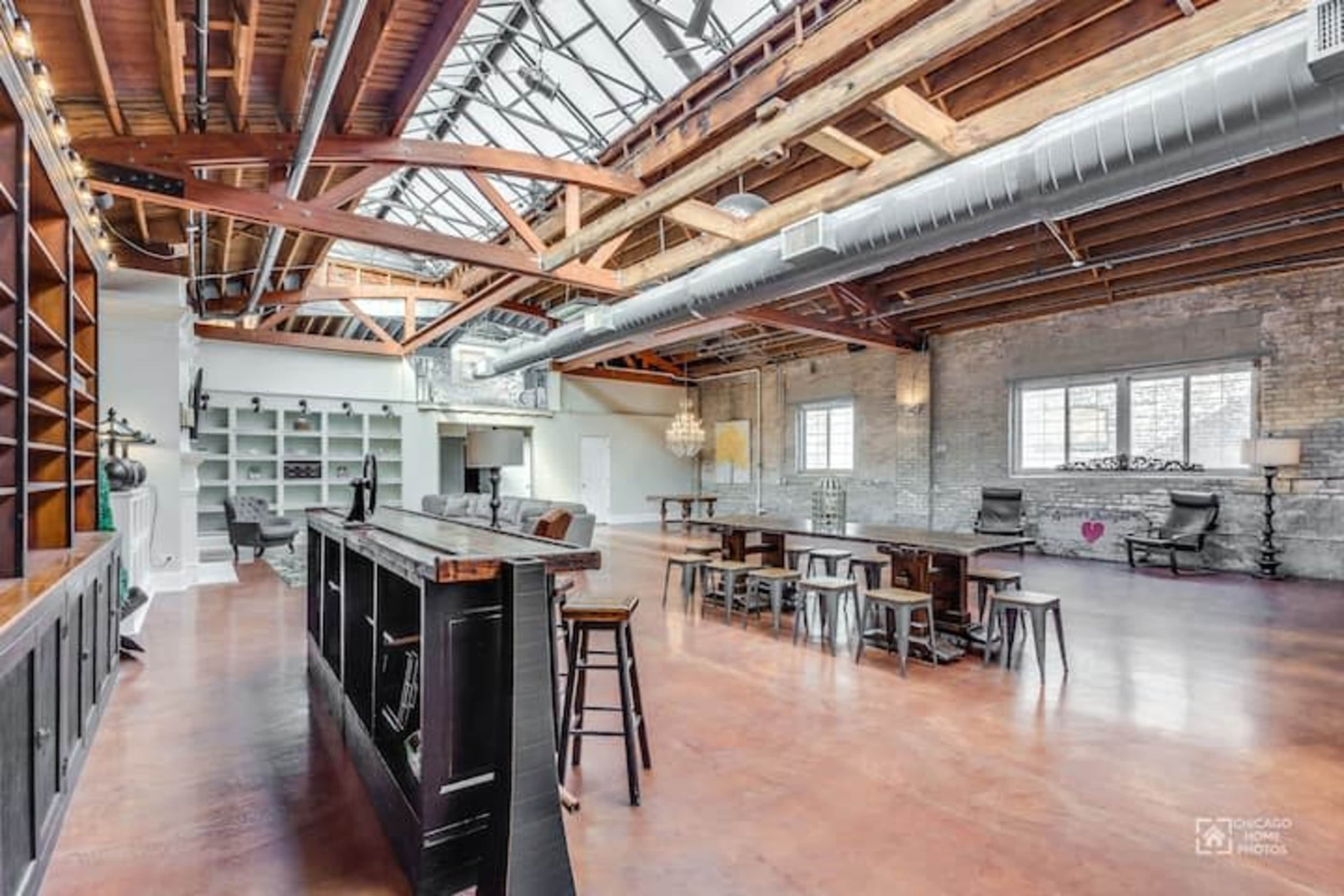 A spacious loft with exposed wooden beams, large windows, and a mix of modern and rustic furniture.