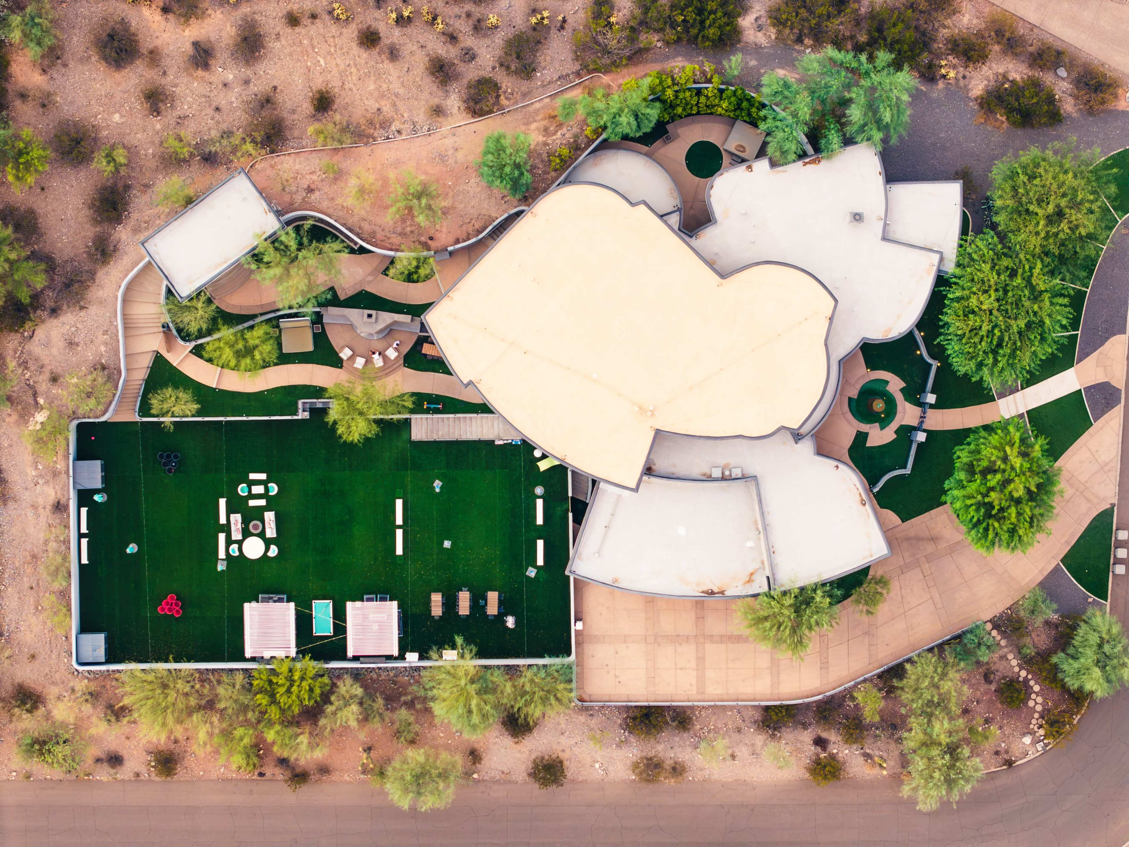 The image shows an aerial view of a uniquely shaped building surrounded by landscaped green areas and pathways.