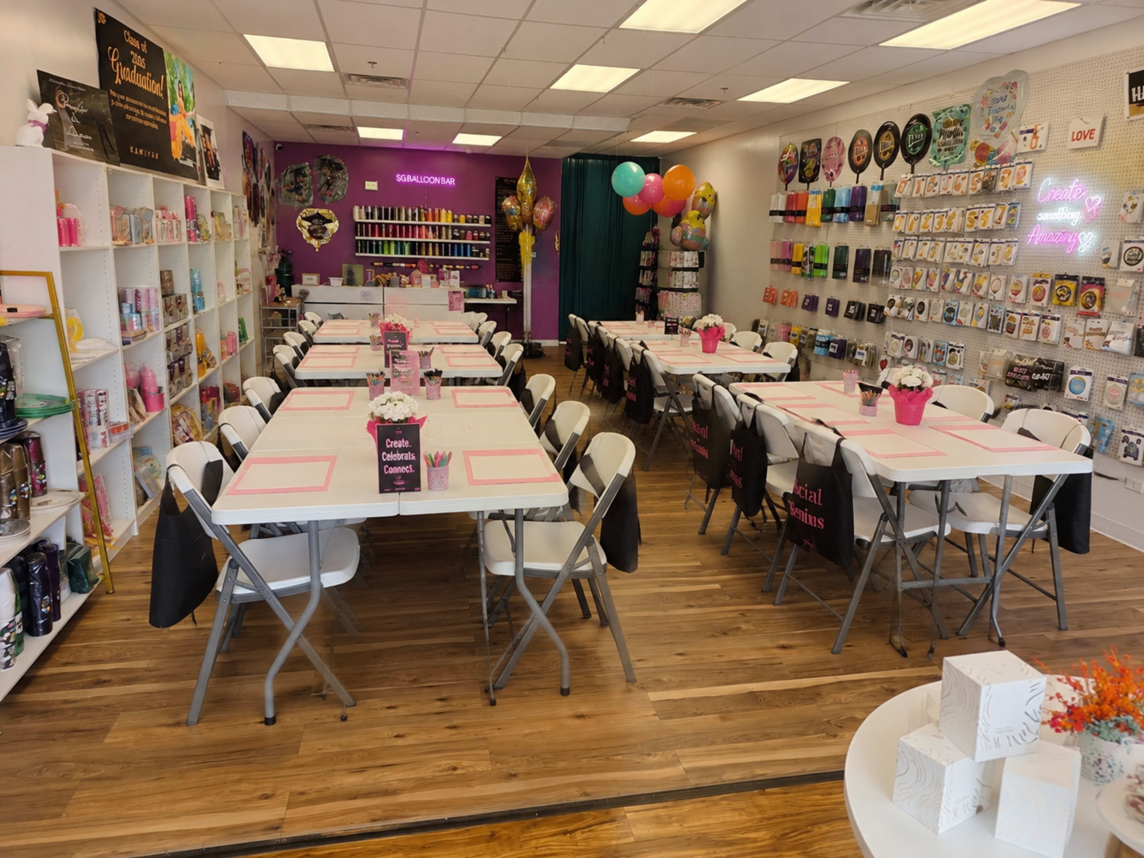 The image shows a colorful event space with tables set for a gathering, surrounded by decorative items and party supplies on display.