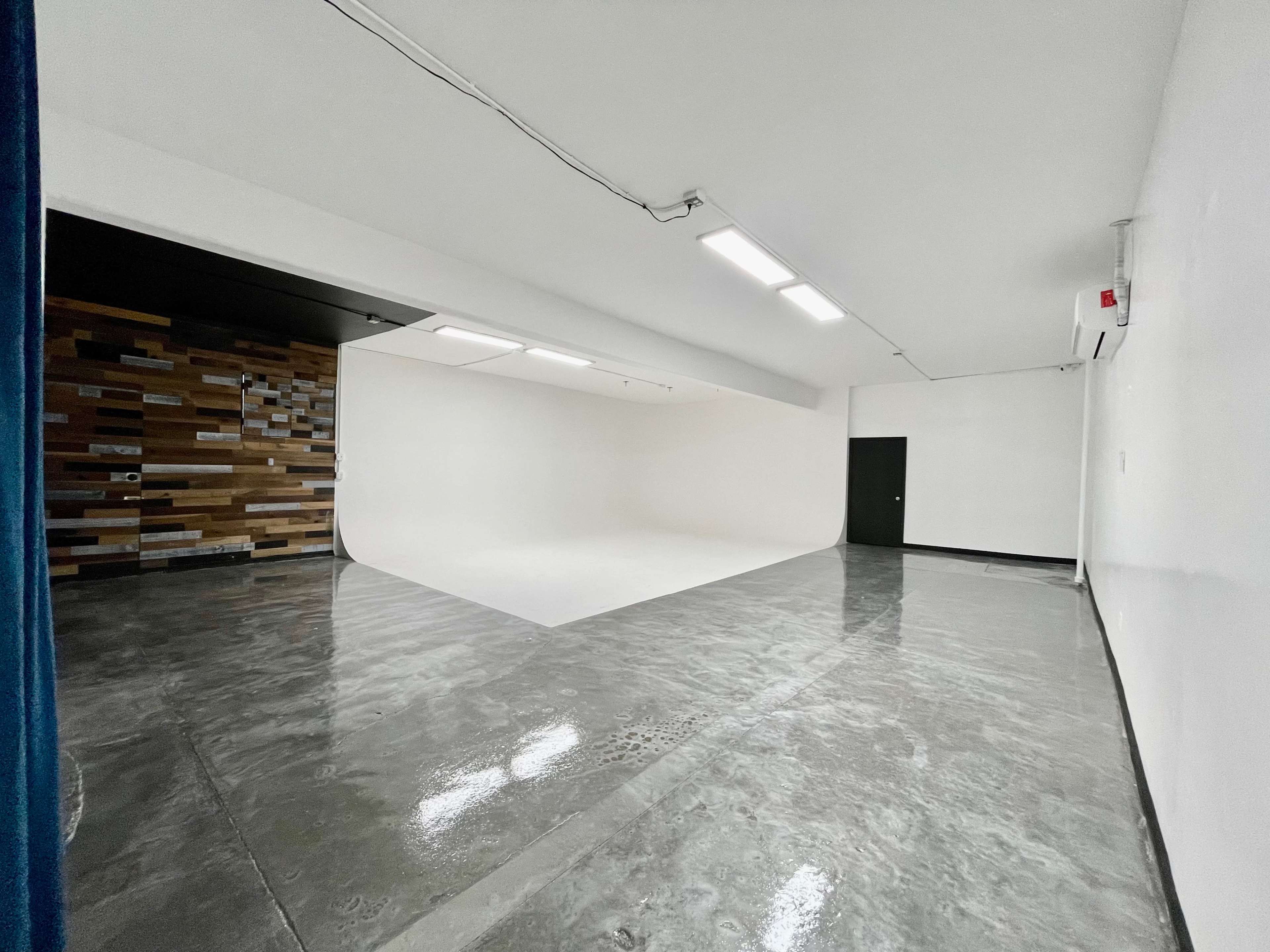A minimalist studio space with a curved white backdrop and a polished concrete floor.