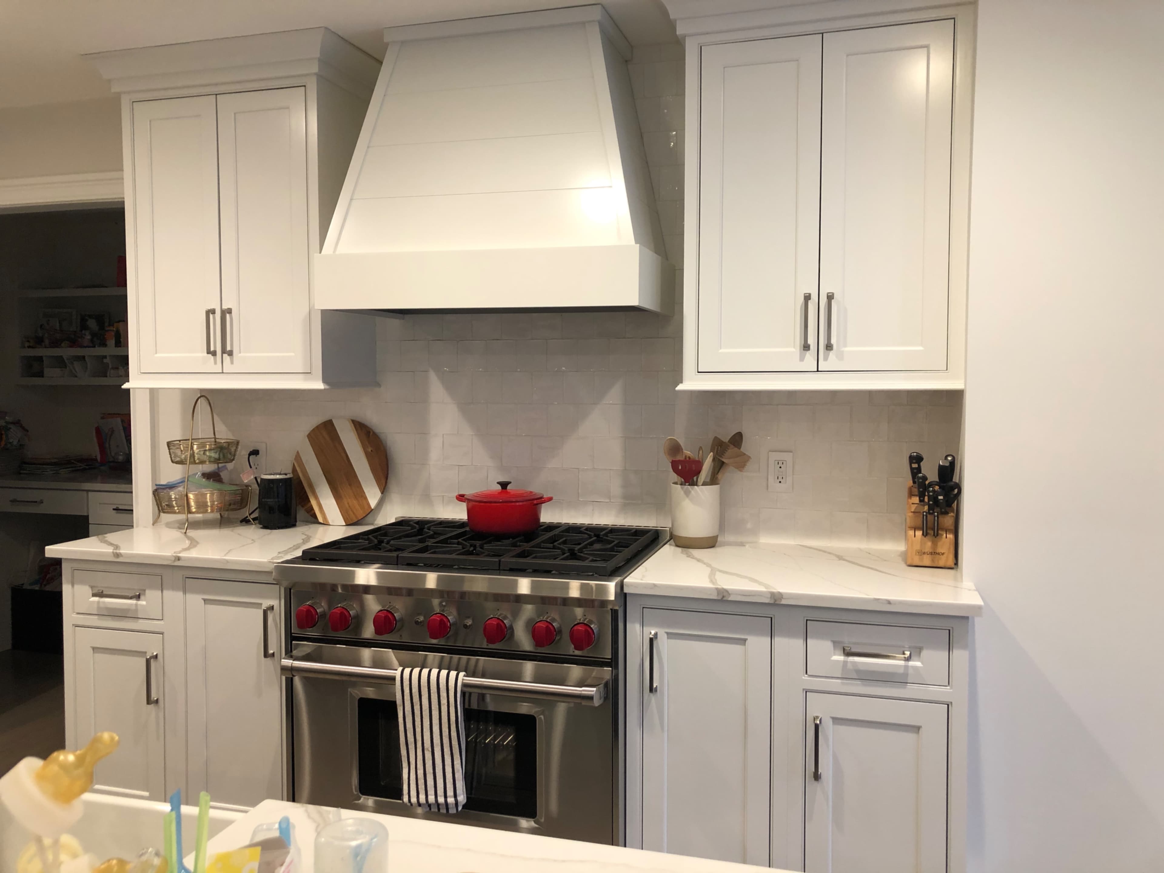 A modern kitchen featuring white cabinetry, a large stainless steel oven range, a red pot on the stove, and a marble countertop.