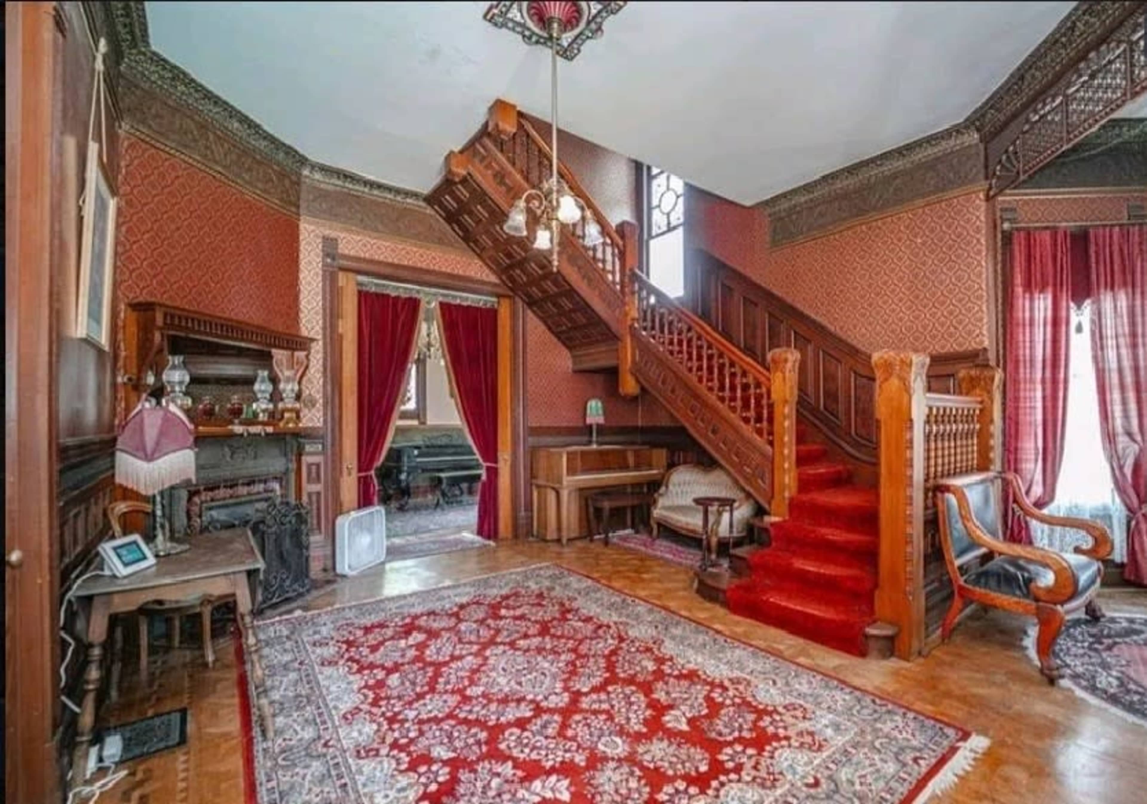 A Victorian-style foyer with a wooden staircase, patterned wallpaper, and a red carpet.