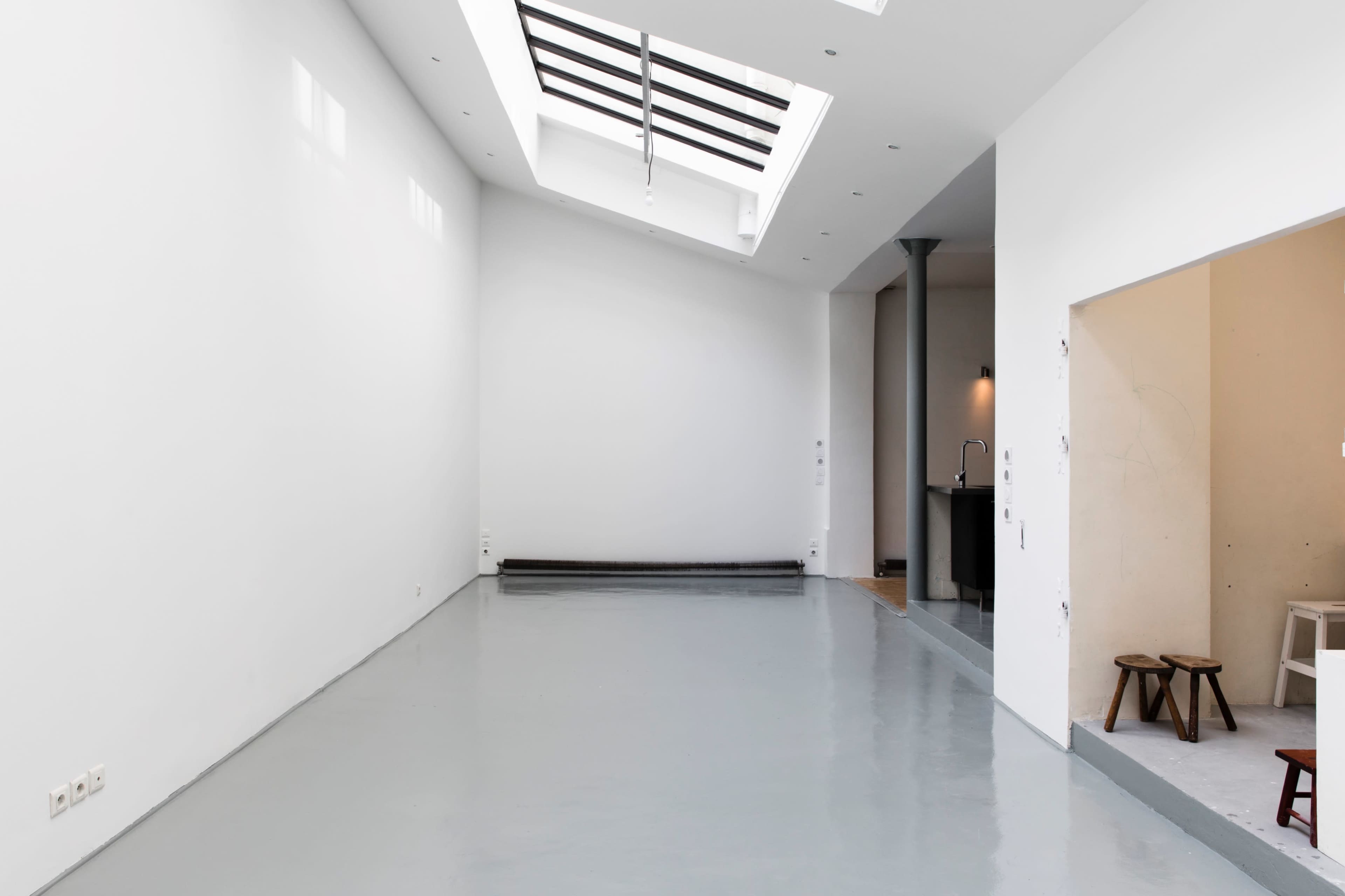 A spacious, minimalist room with a skylight, polished gray floor, and an adjoining area that features a small kitchen nook.