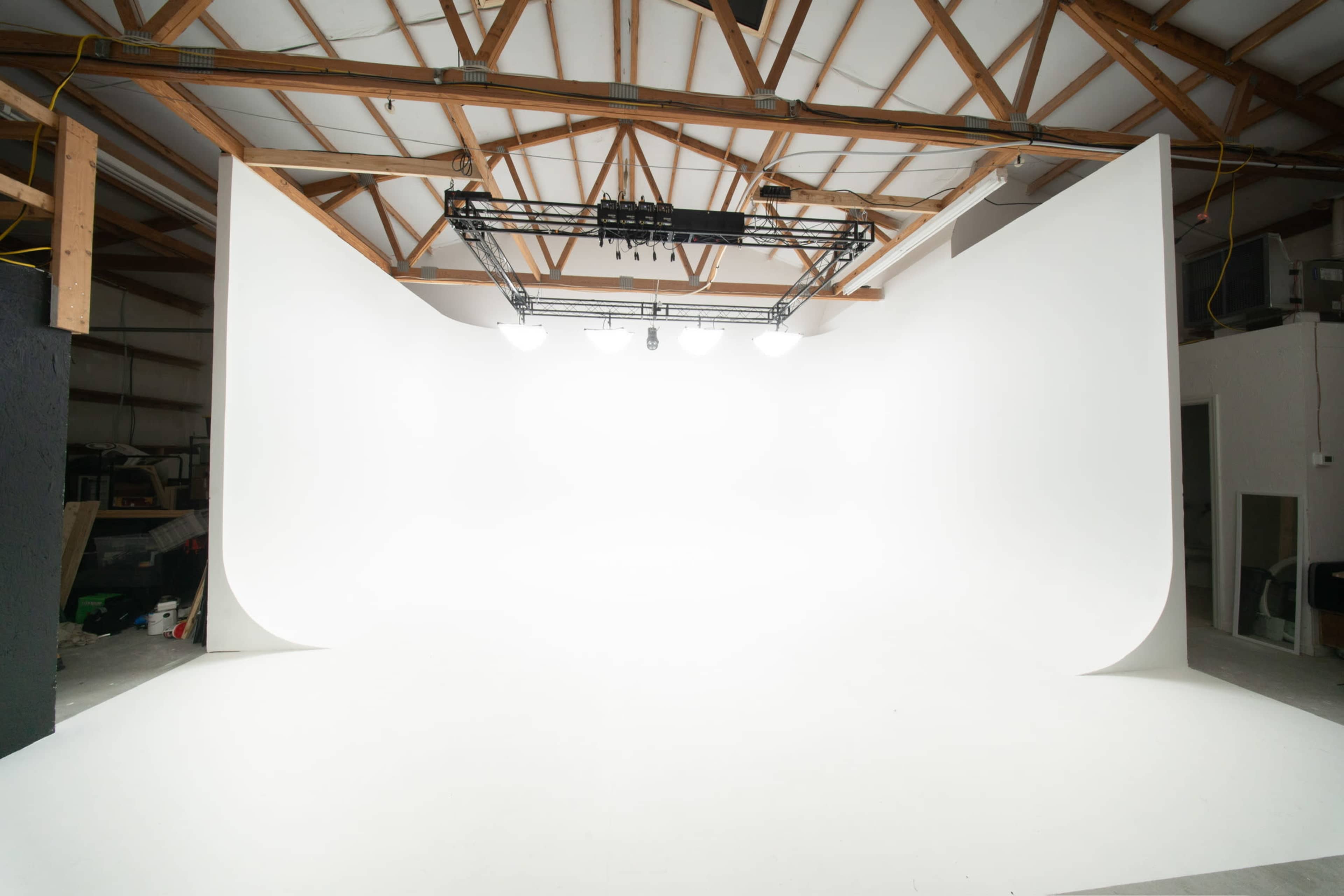 The image shows a photography studio featuring a large white seamless backdrop and a grid of overhead lights.