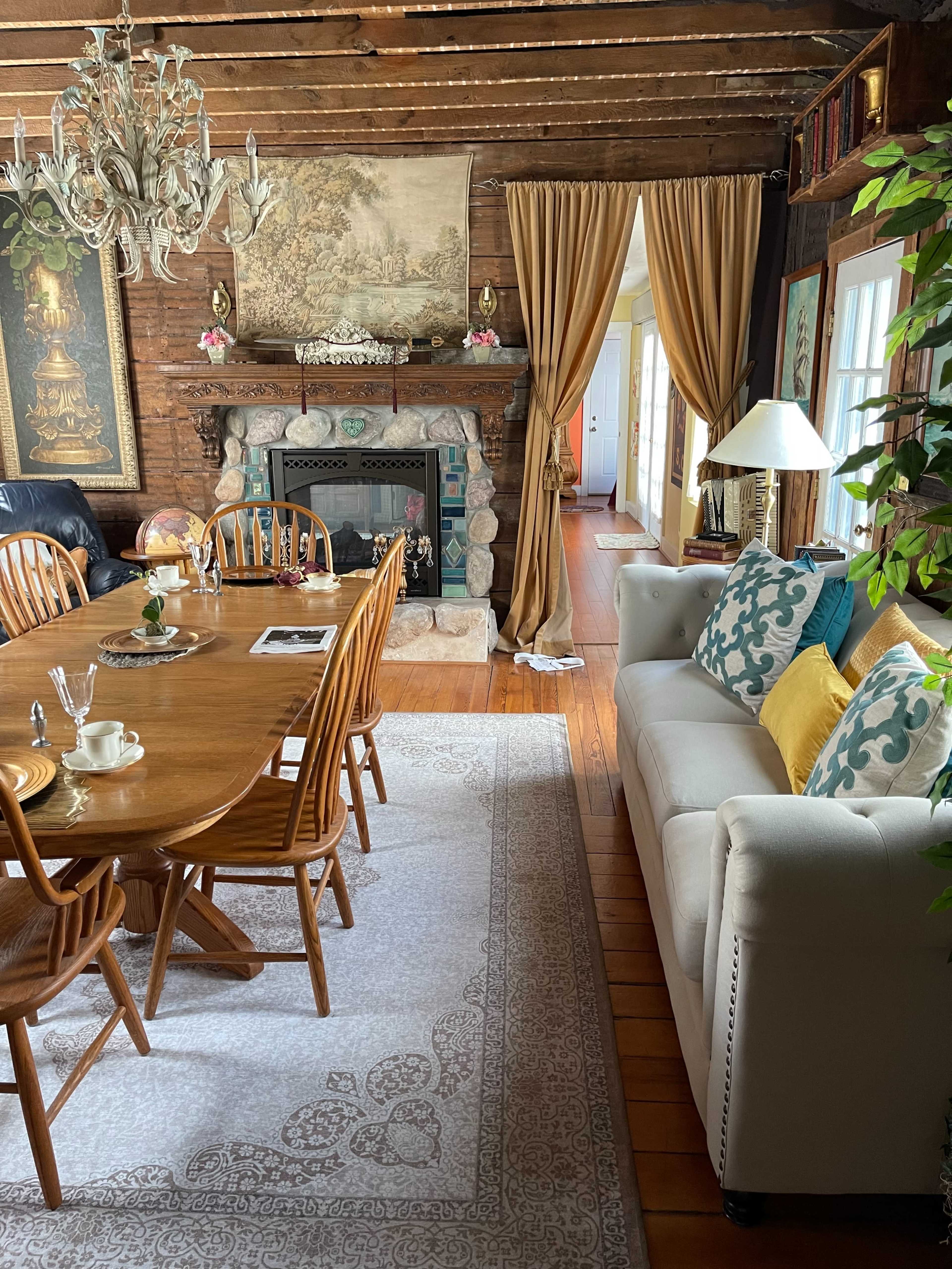 A dining area features a wooden table with chairs, a stone fireplace, and a cozy seating arrangement with decorative pillows.