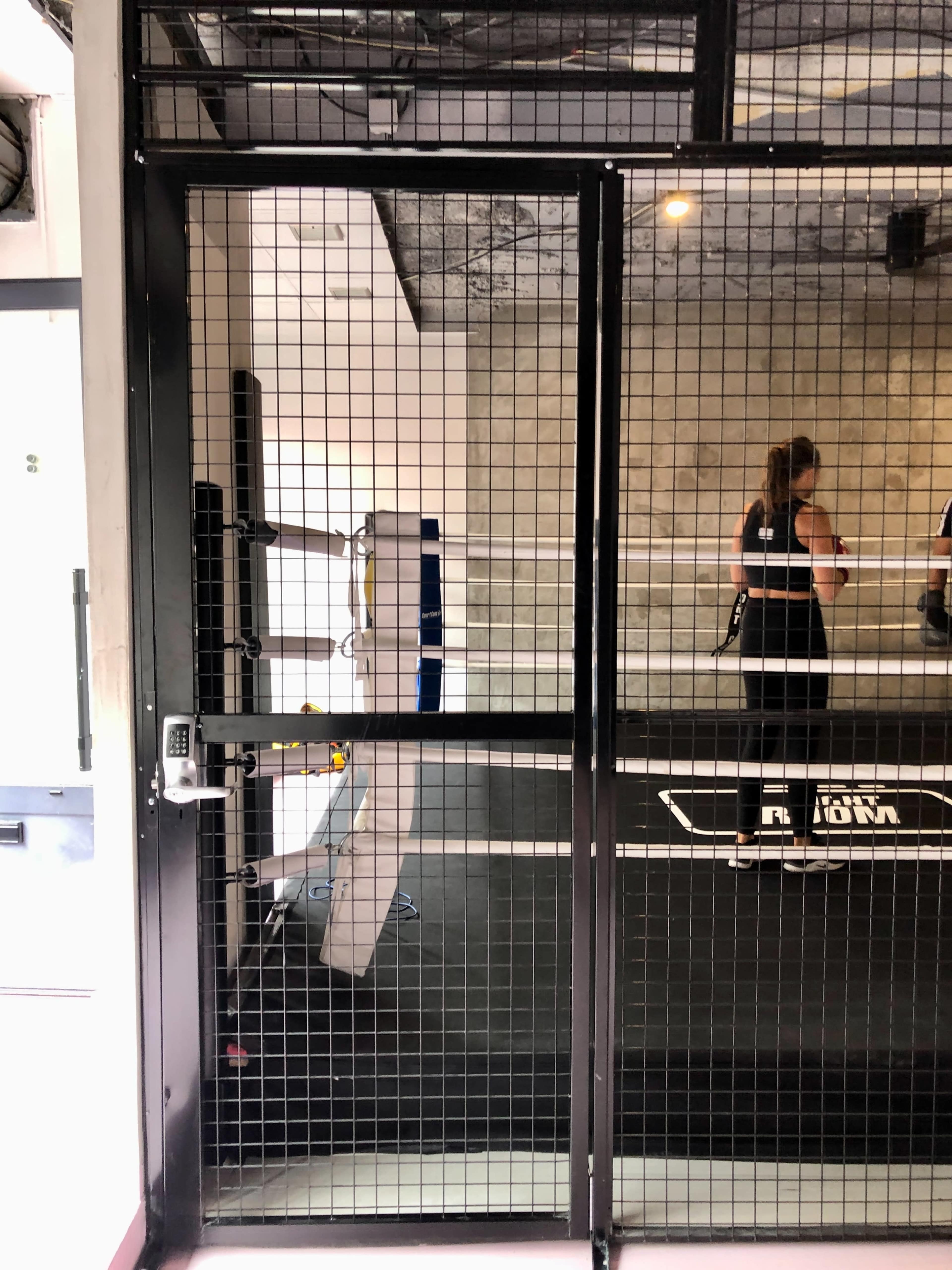 The image shows a fenced entrance to a gym area, with a mirrored wall and workout equipment visible inside.