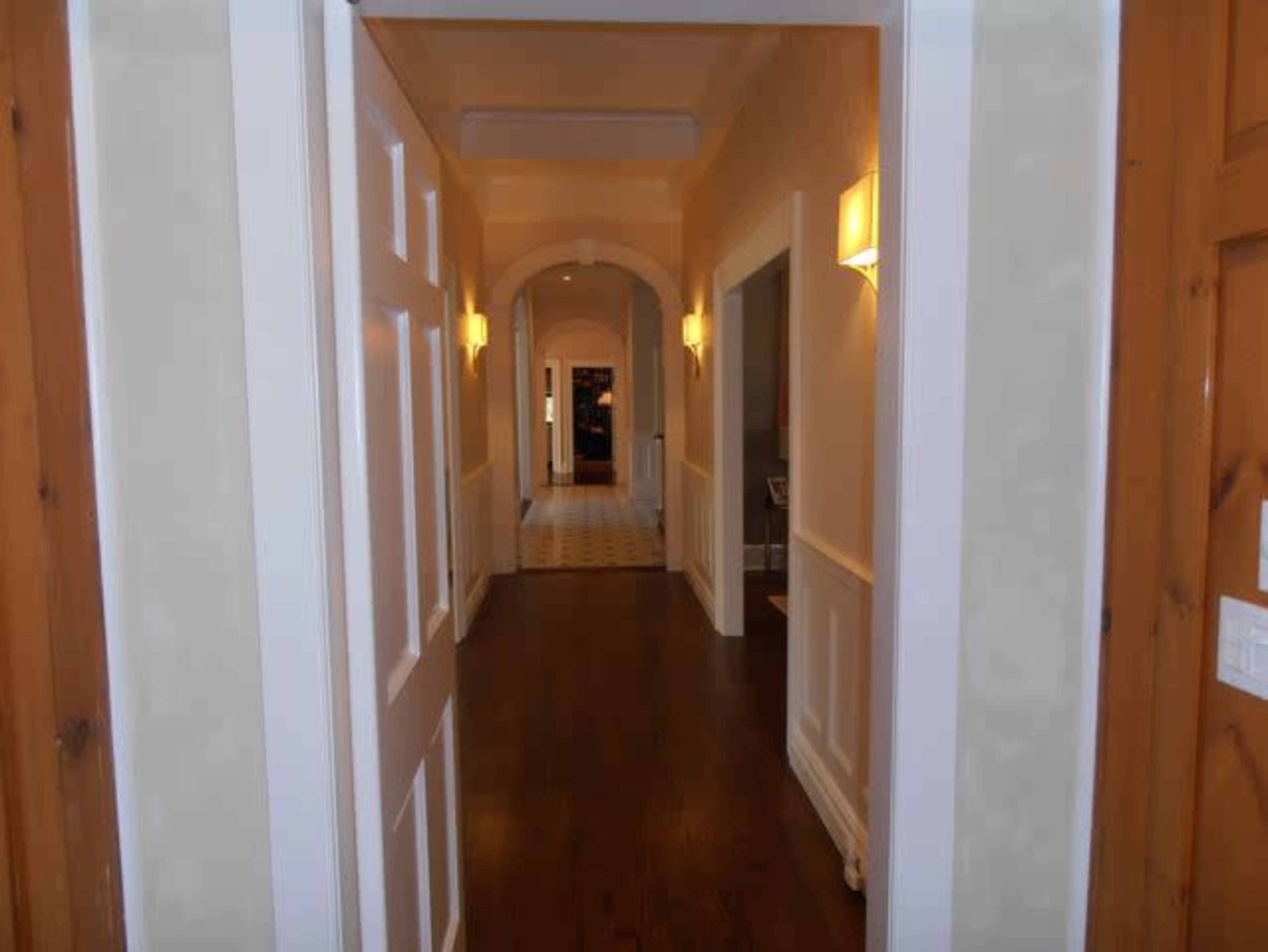 A hallway with wooden flooring and walls painted in light colors leads to an arched doorway at the end.