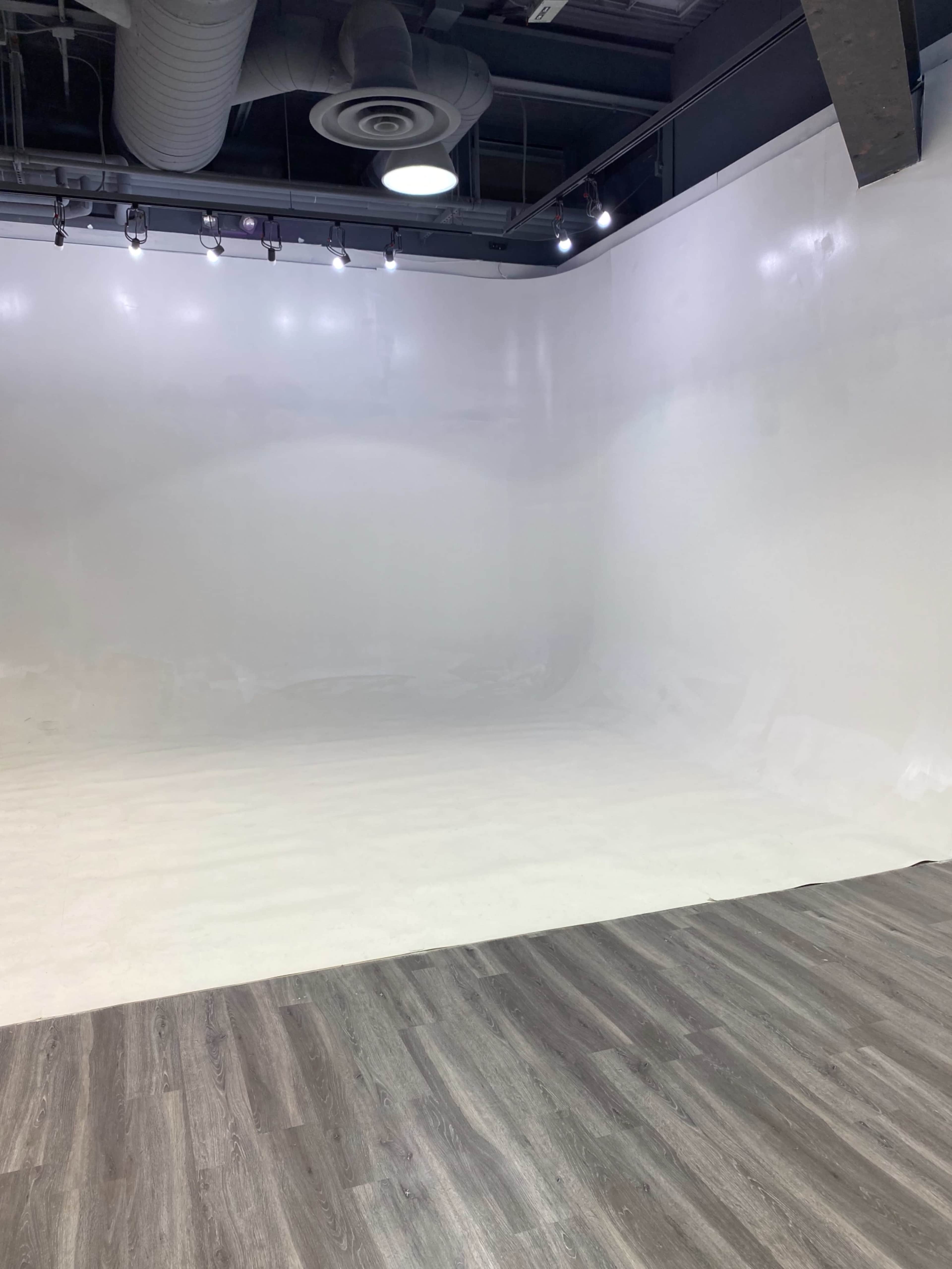A spacious, empty studio with white walls and a light-colored wooden floor.