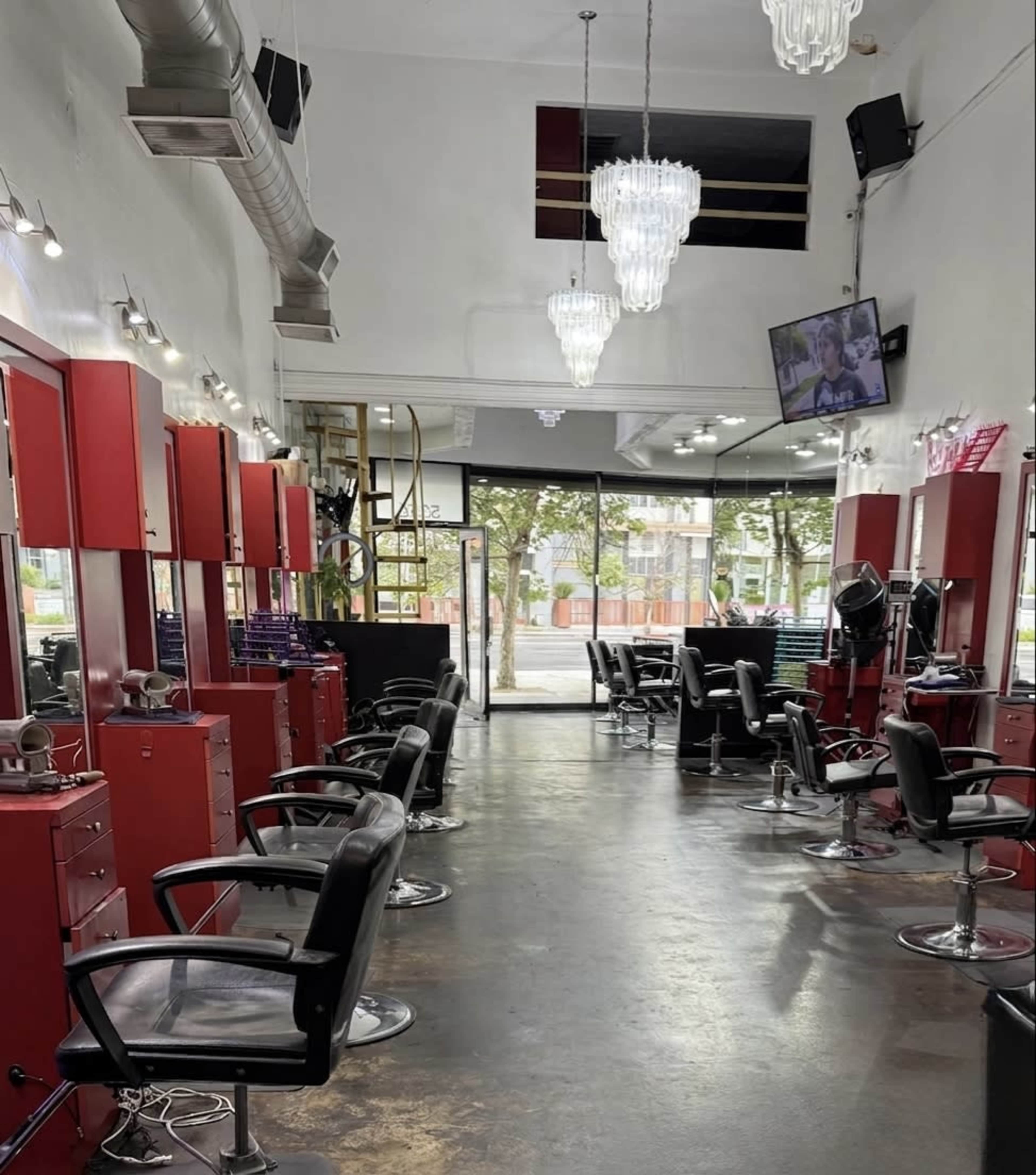 The image shows the interior of a hair salon featuring multiple styling stations with red cabinets and black chairs, illuminated by chandelier lights.