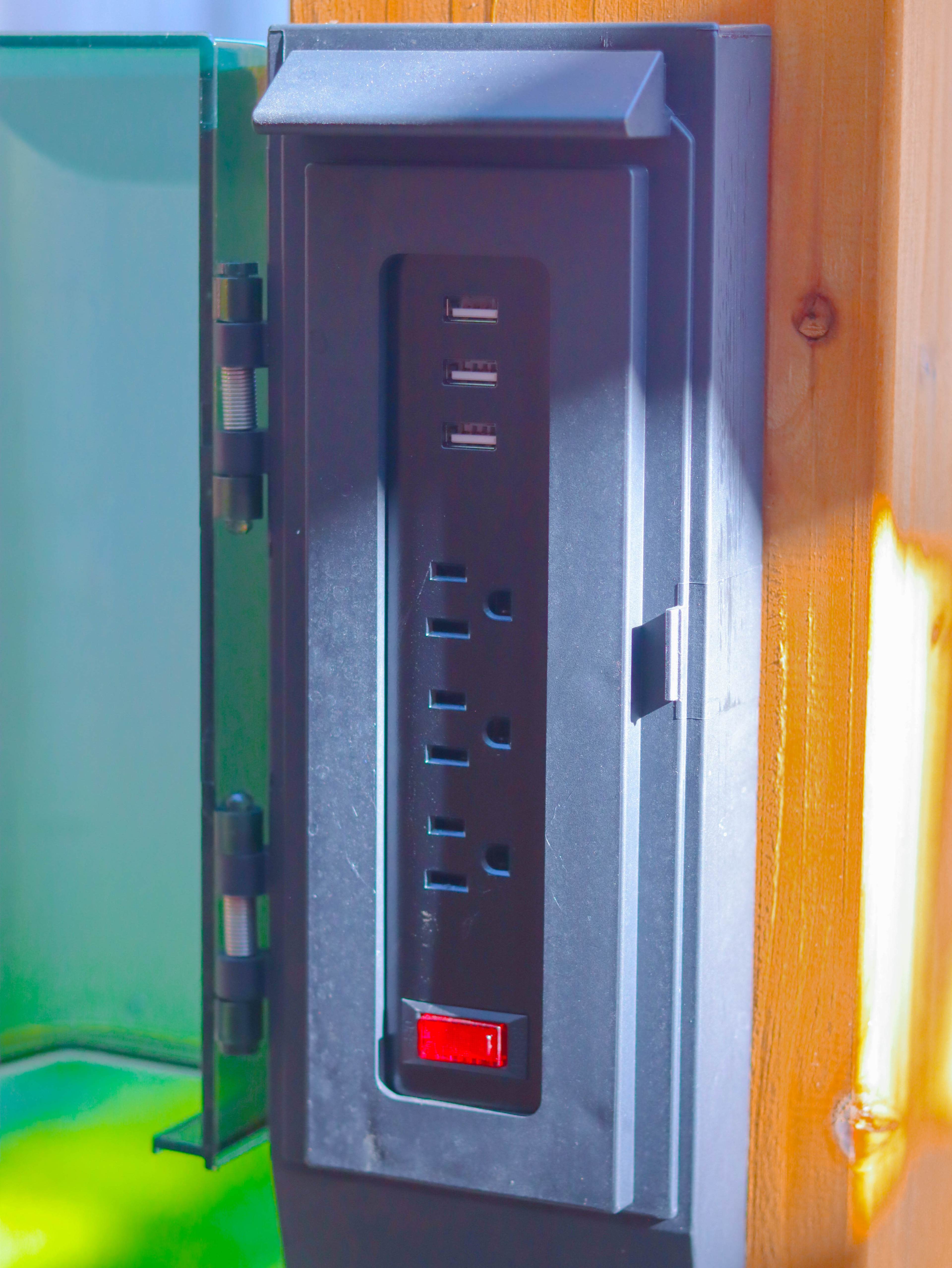 A mounted power outlet with multiple USB ports and a switch, situated against a wooden background.
