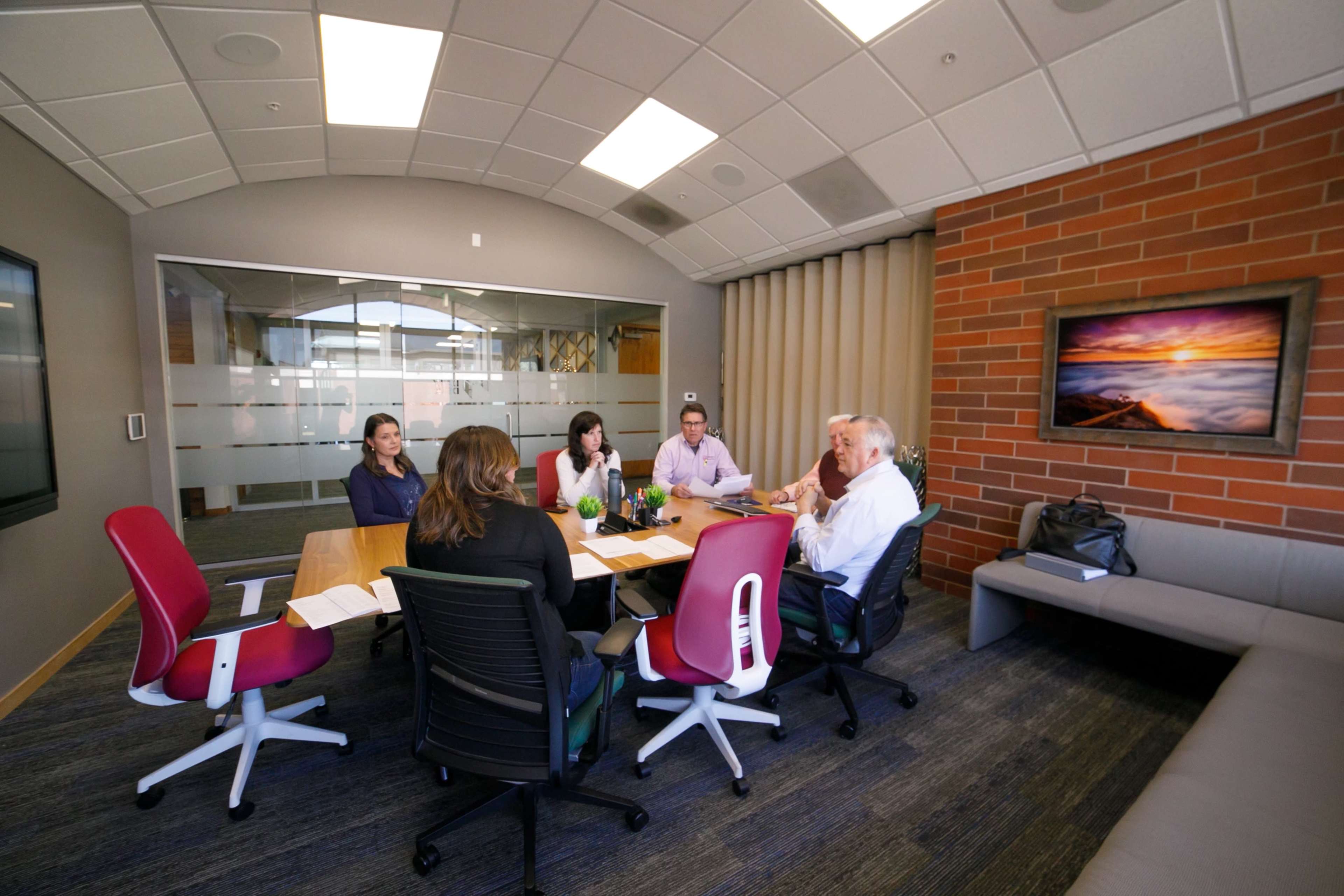 A group of five people is seated around a conference table in a modern meeting room.