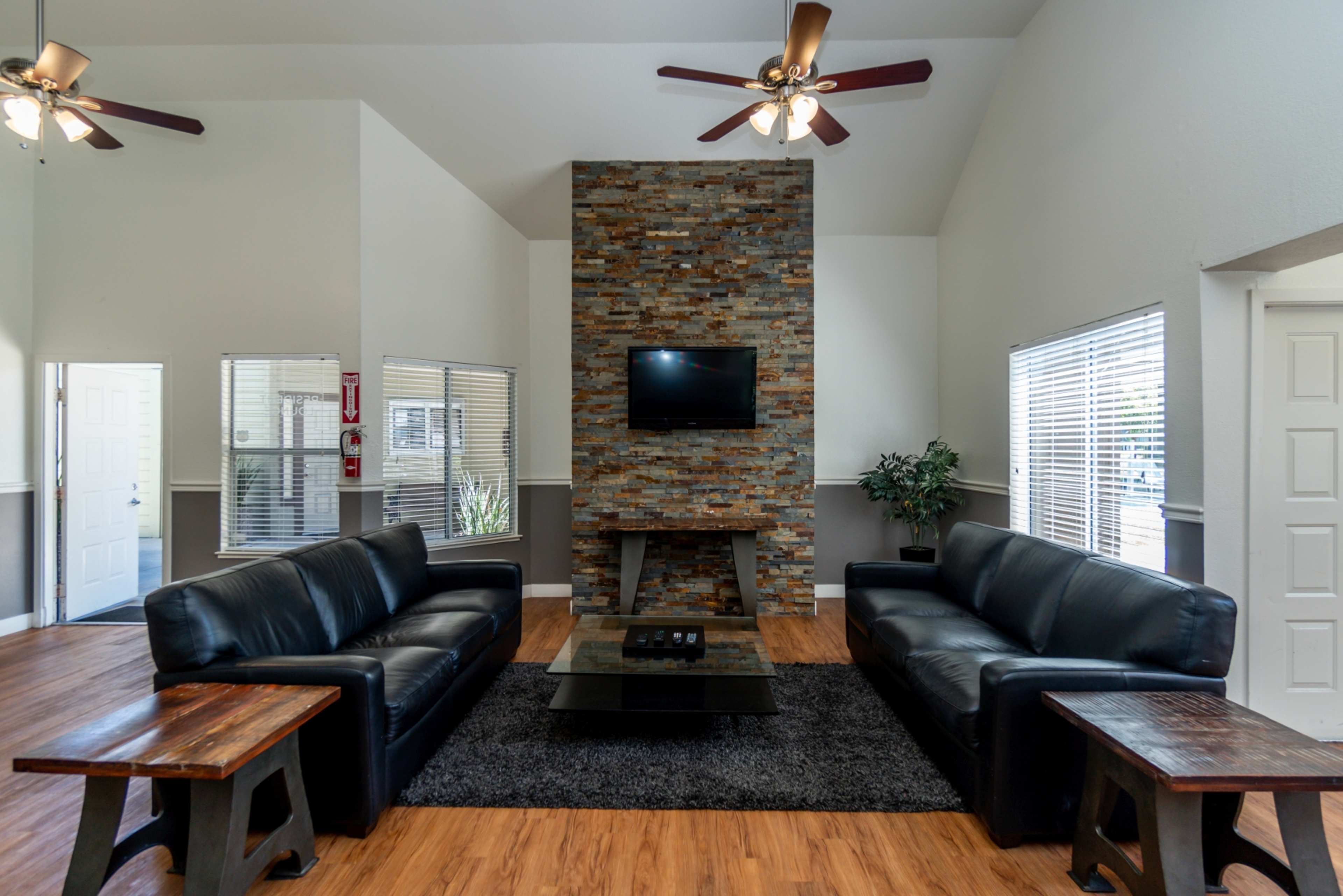 A modern living room featuring two black leather sofas, a coffee table, and a stone fireplace with a mounted television.