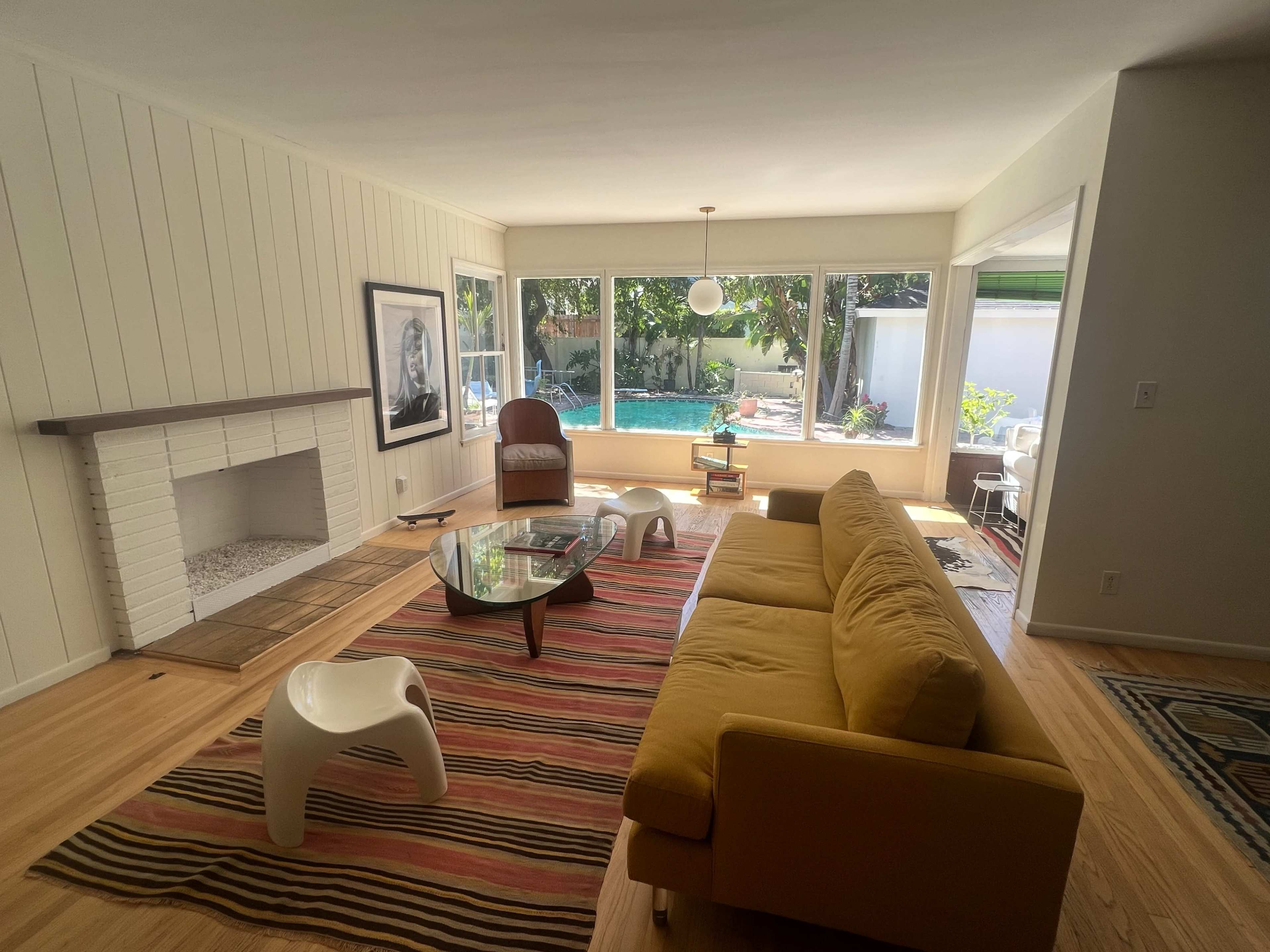 The living room features a mustard-colored sofa, a glass coffee table, and a view of an outdoor terrace through large windows.