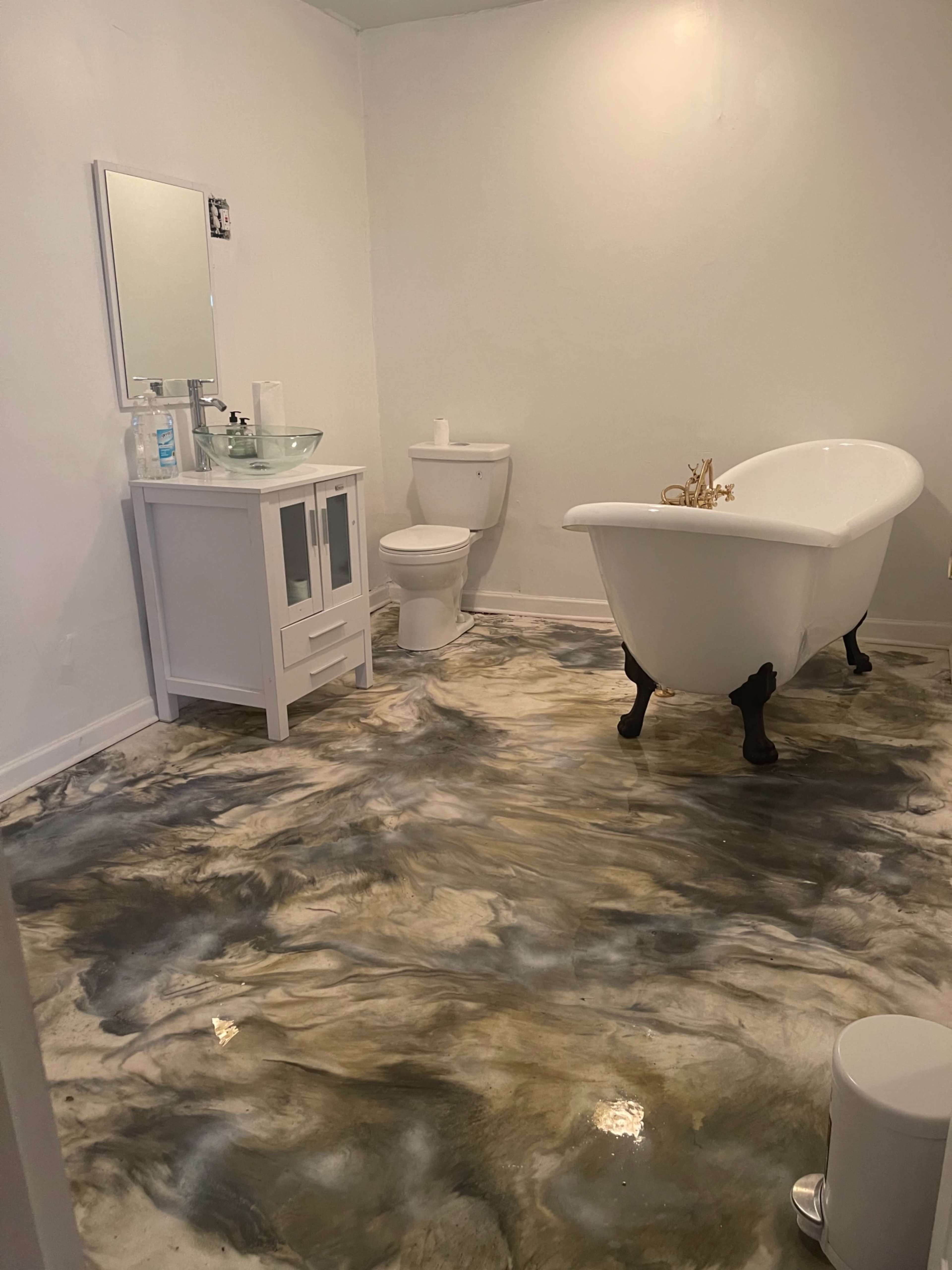 The bathroom features a clawfoot bathtub, a toilet, a sink with a cabinet, and a marbled floor design.
