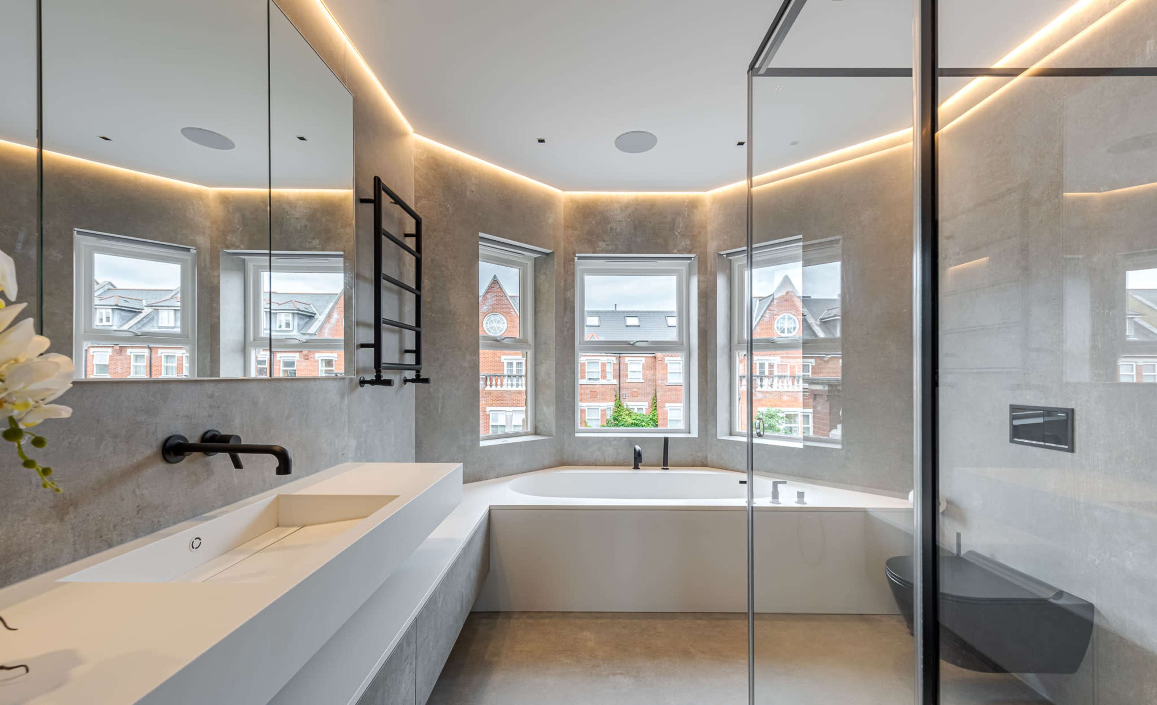 The bathroom features a modern design with a freestanding bathtub, a sleek vanity, multiple windows, and a glass shower enclosure.