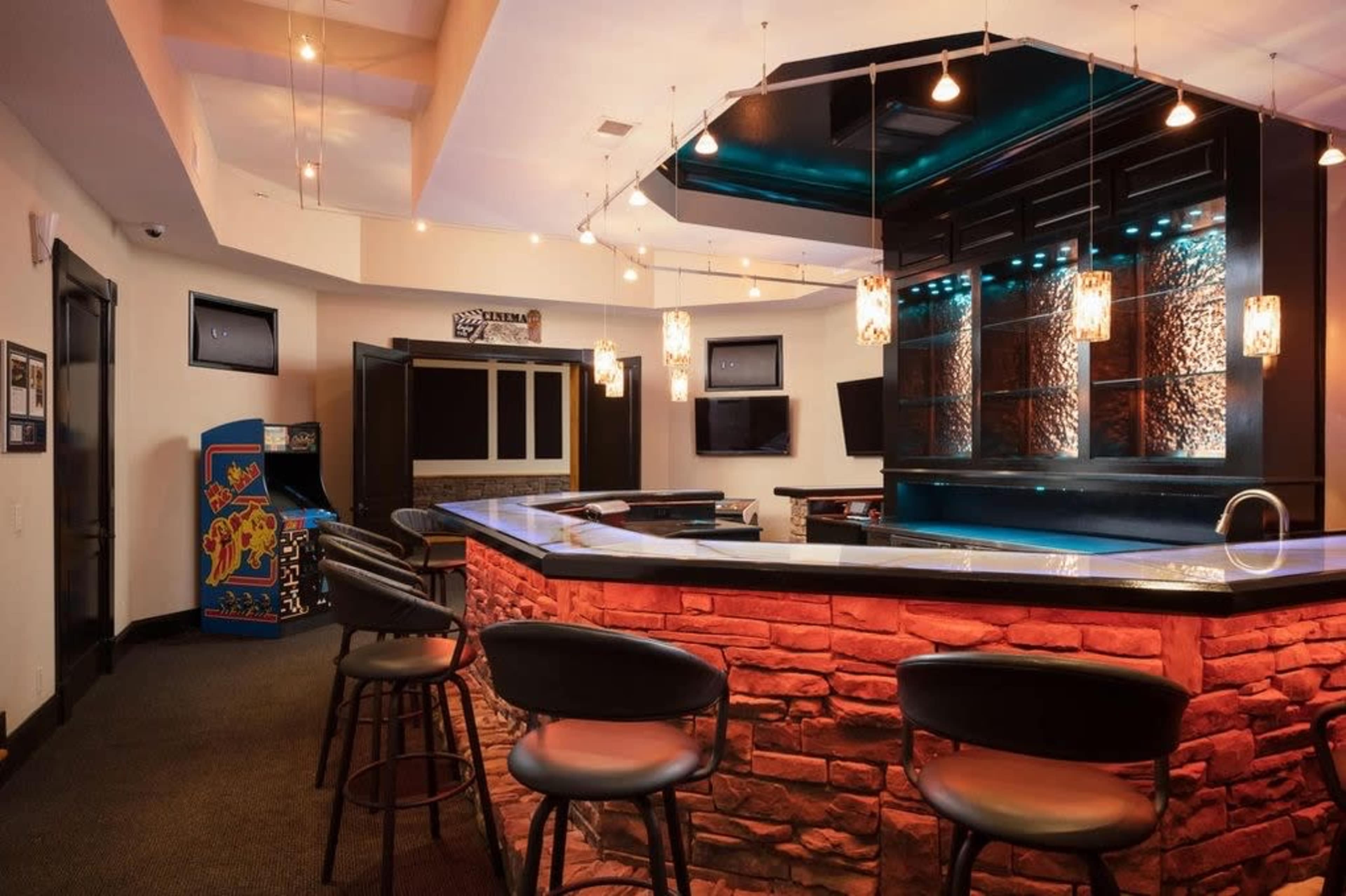 A modern bar area with a stone counter, illuminated pendant lights, and arcade games in the background.