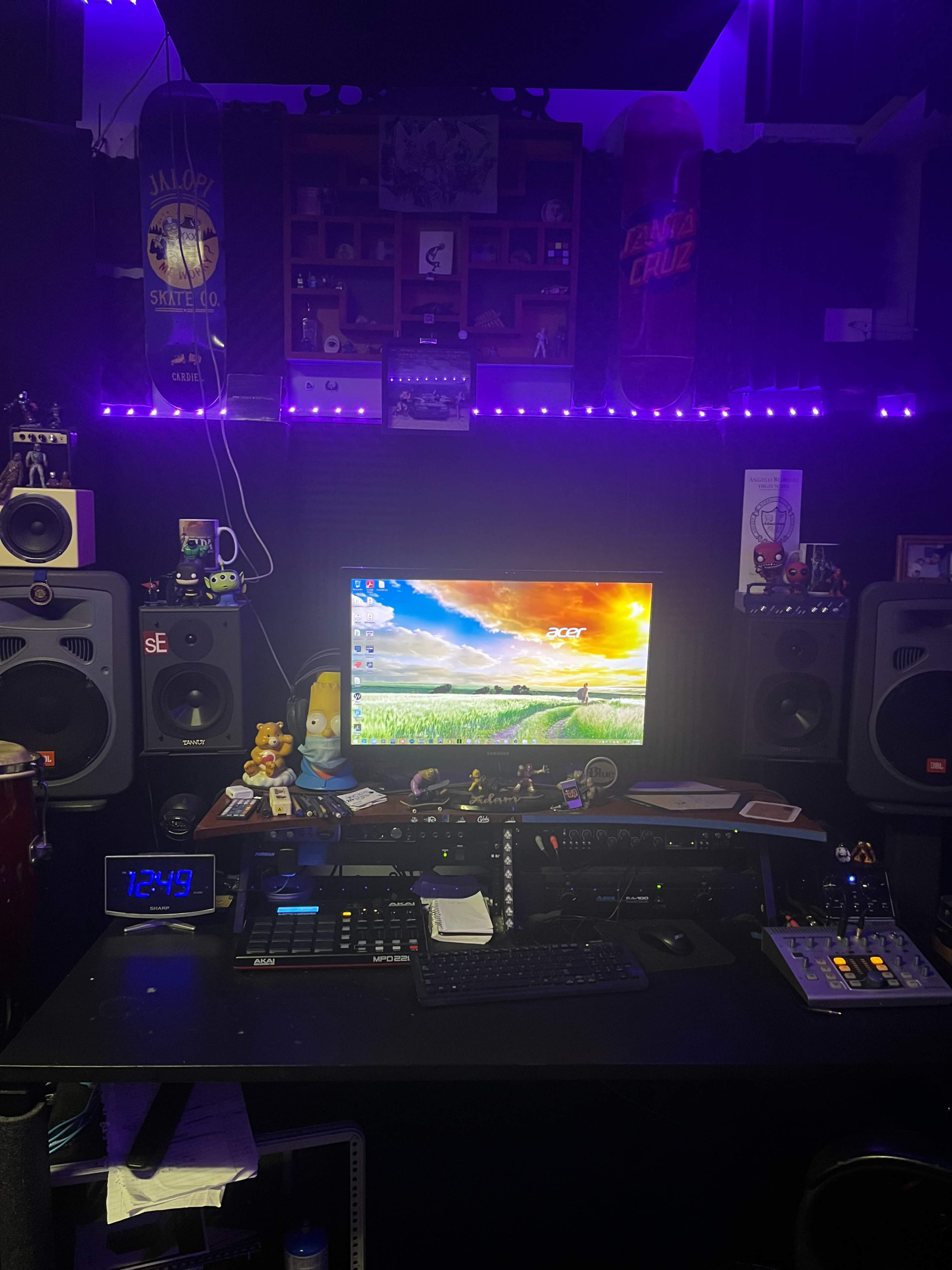 A music production studio setup features a computer monitor, audio equipment, and various decorations under purple LED lights.