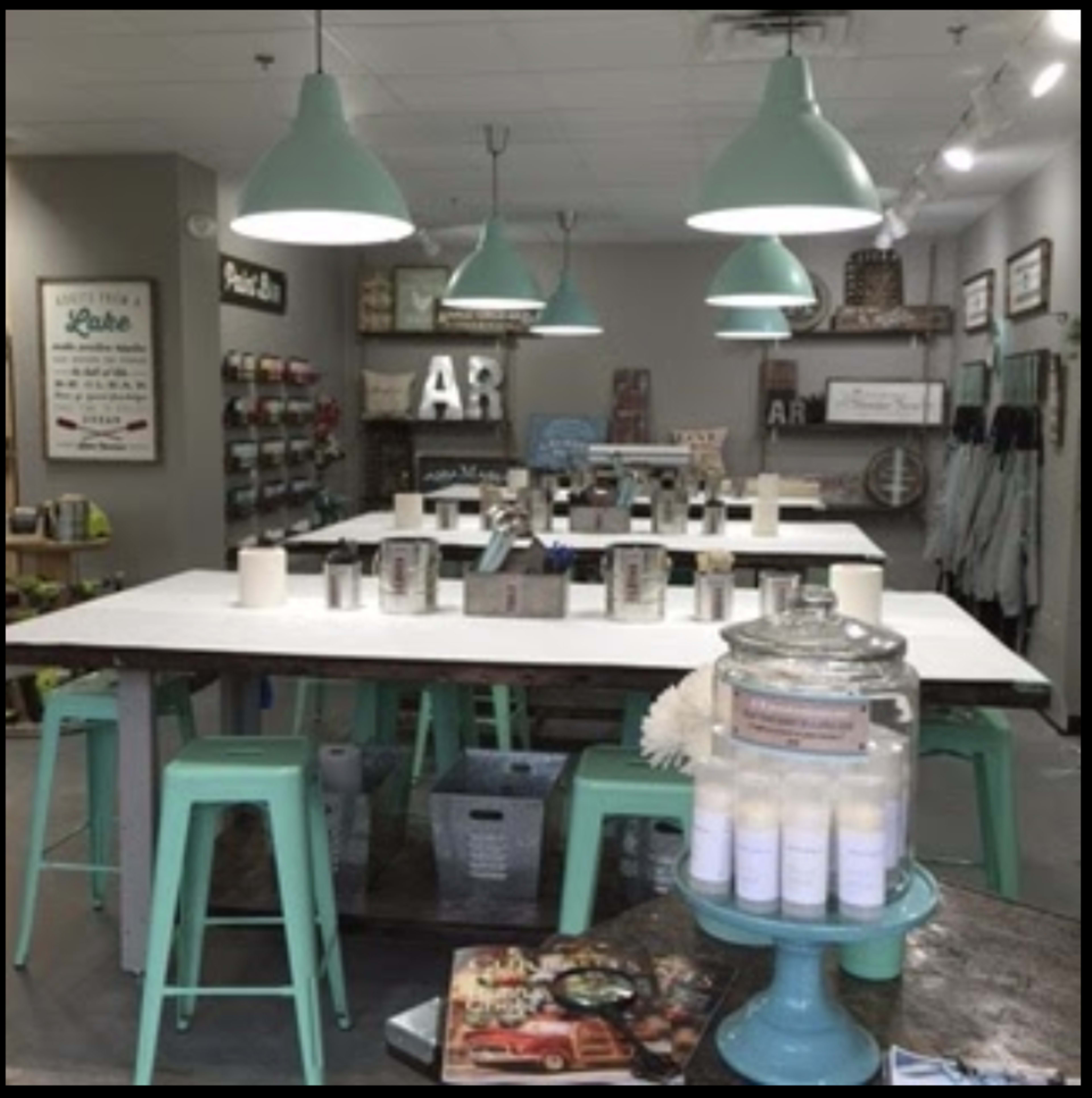 A well-organized workshop space with long tables, teal stools, and various decorative items displayed on shelves and counters.
