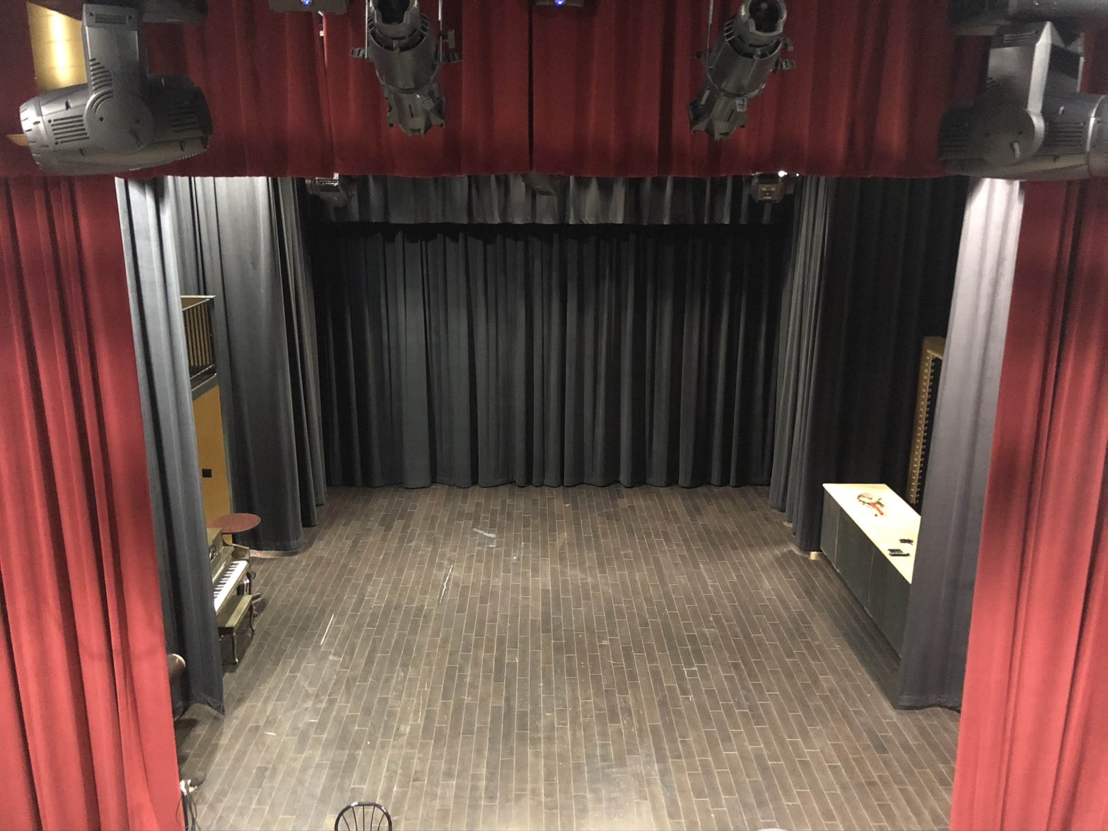 The image shows an empty stage with red curtains, dark walls, and spotlights overhead.