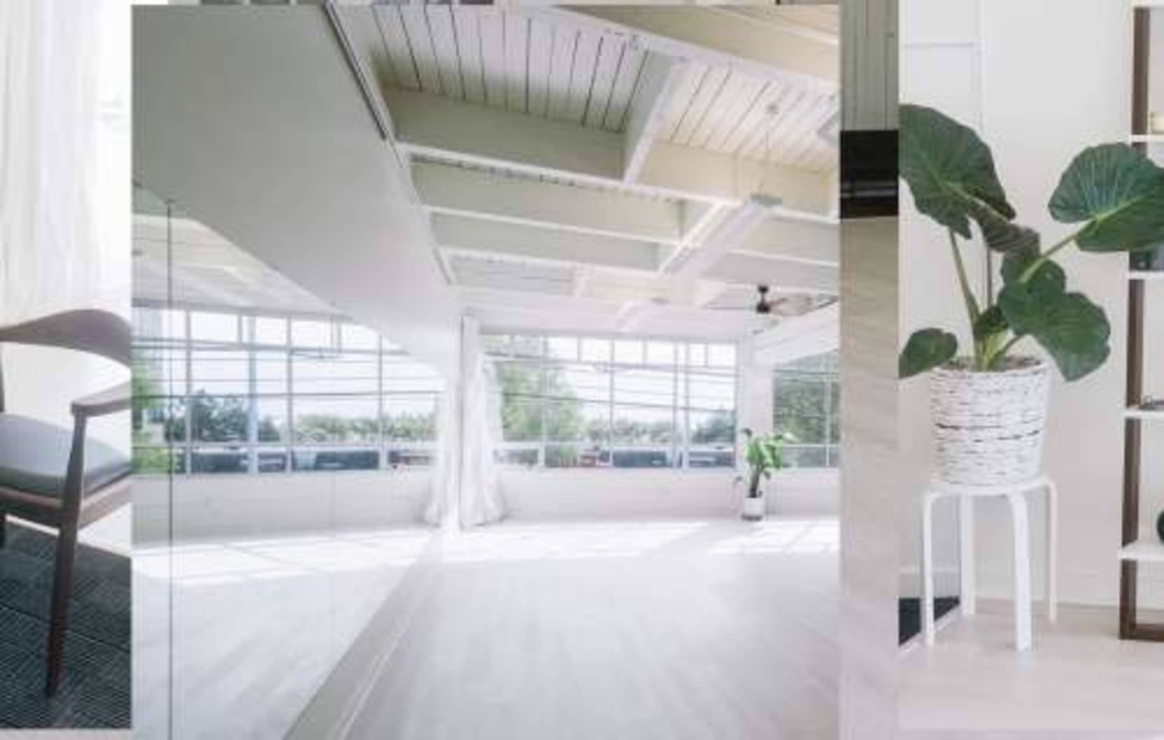A bright, open space with large windows, white walls, and modern furnishings, including a chair and a potted plant.