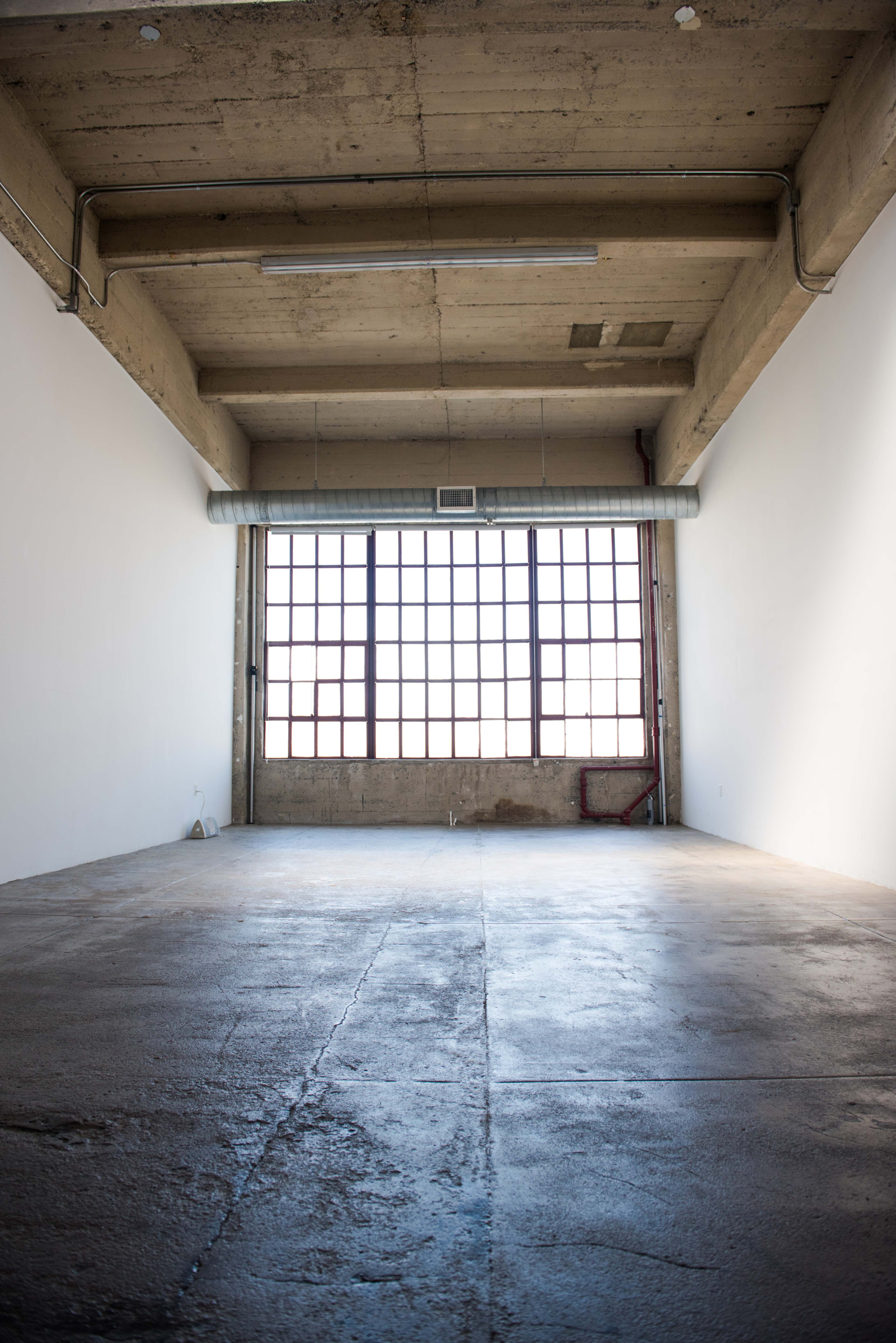 An empty industrial room with a large window and exposed concrete ceilings.