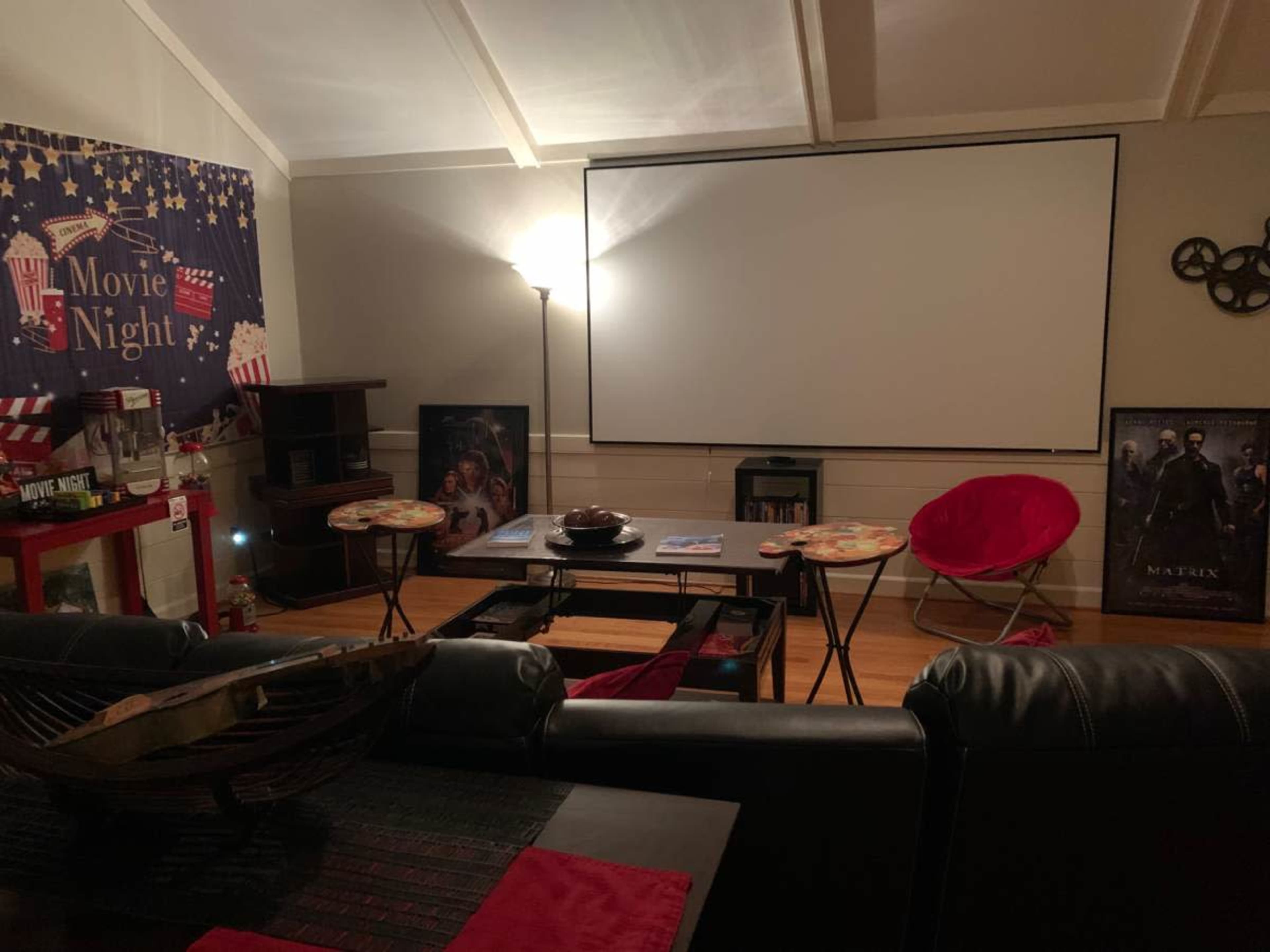 The image shows a cozy home theater setup with a large projector screen, seating area, and movie-themed decorations including popcorn and film posters.