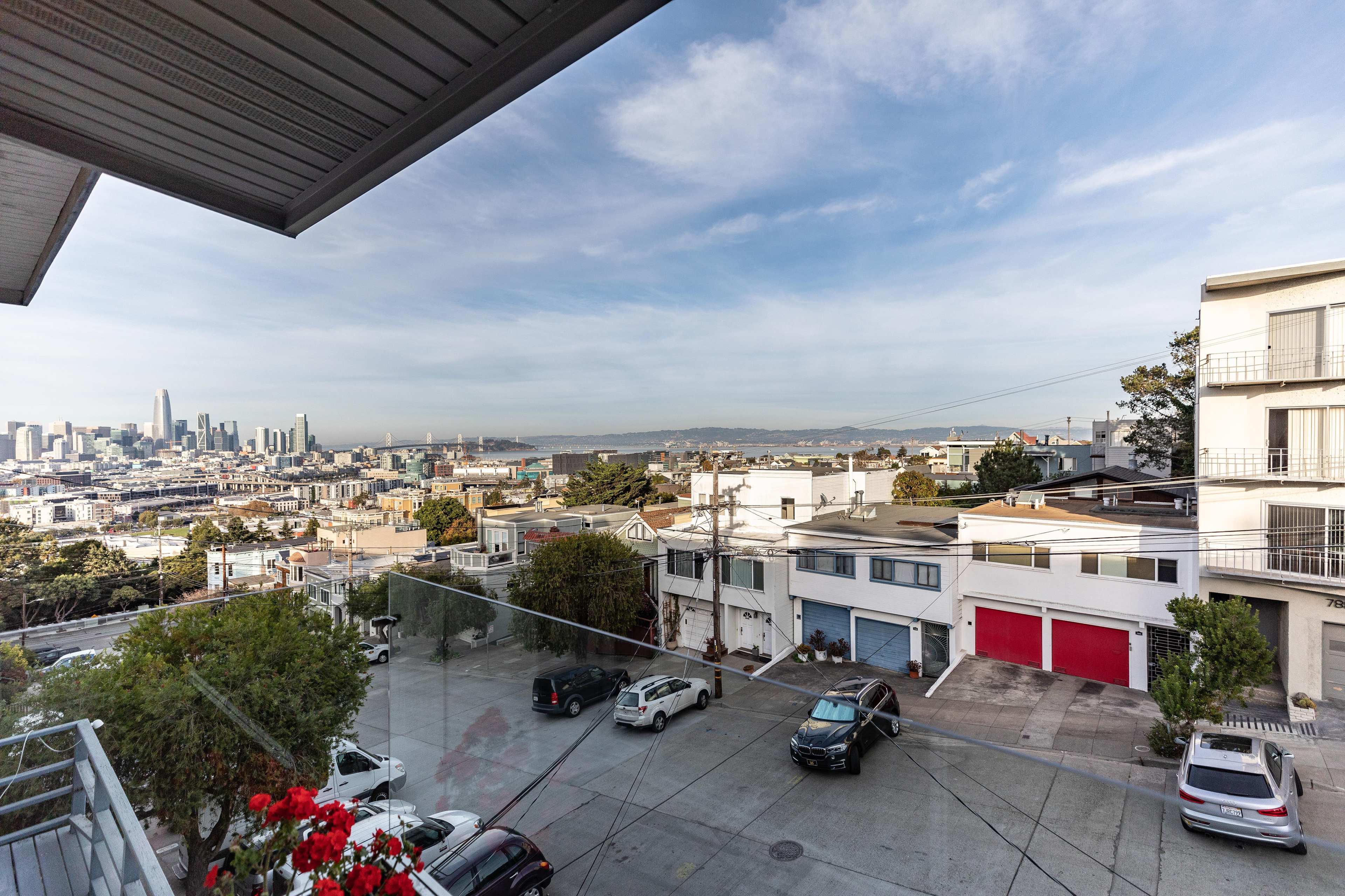 A view from an apartment balcony overlooking a cityscape with buildings, parked cars, and the San Francisco skyline in the background.