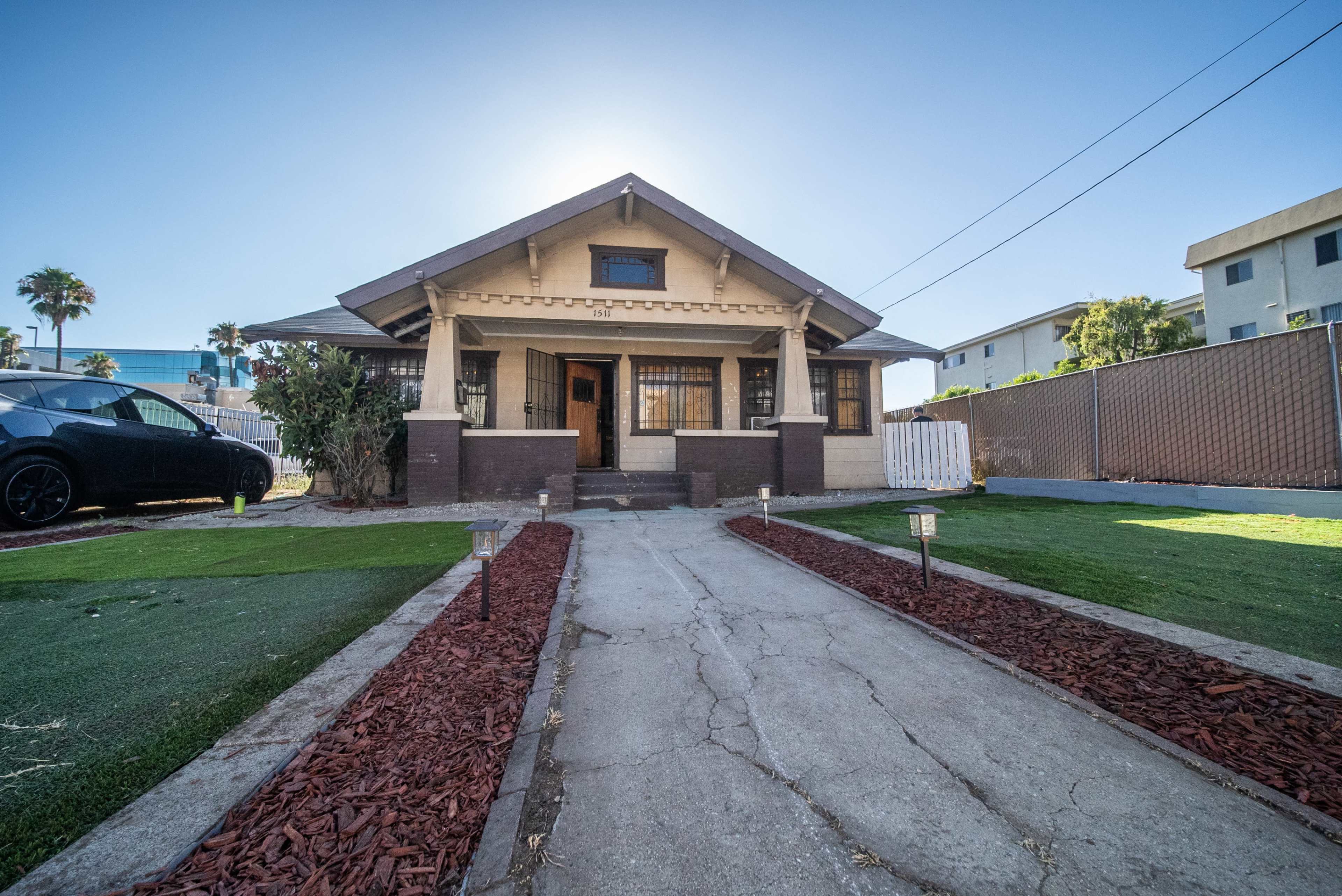 A single-story bungalow with a front walkway surrounded by landscaped grass and mulch, situated in an urban setting.