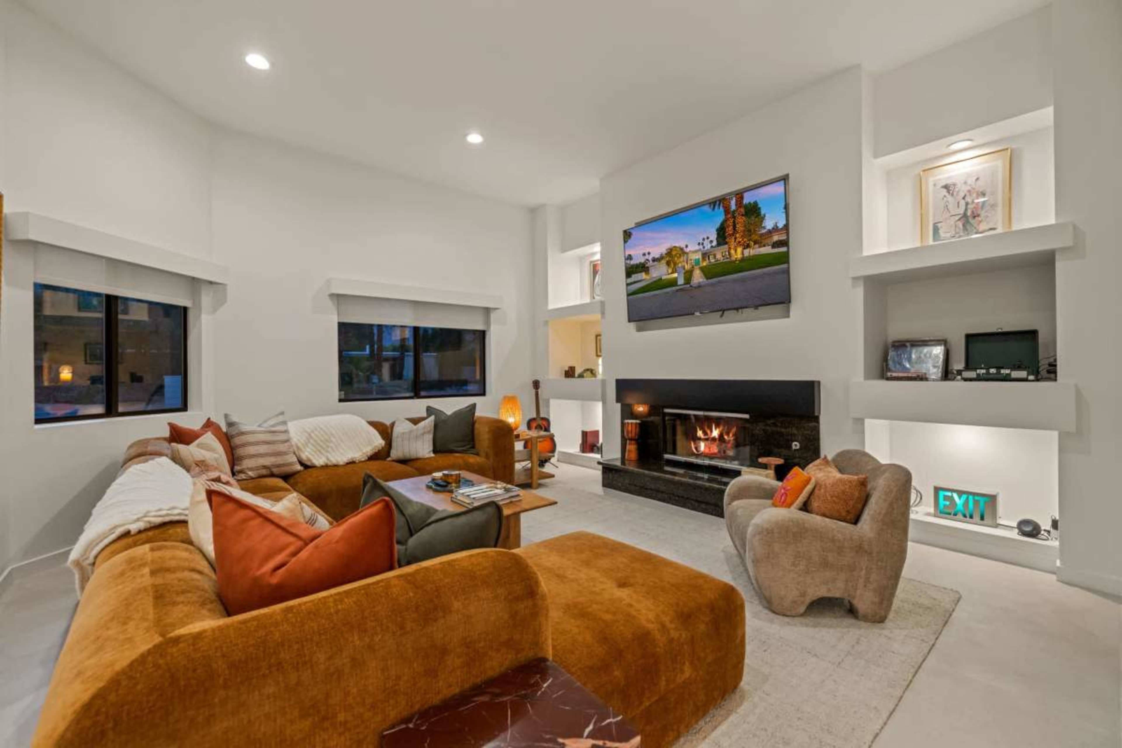 The image shows a modern living room with a large sectional sofa, a fireplace, and a mounted television, all arranged in a well-lit space with minimalistic decor.