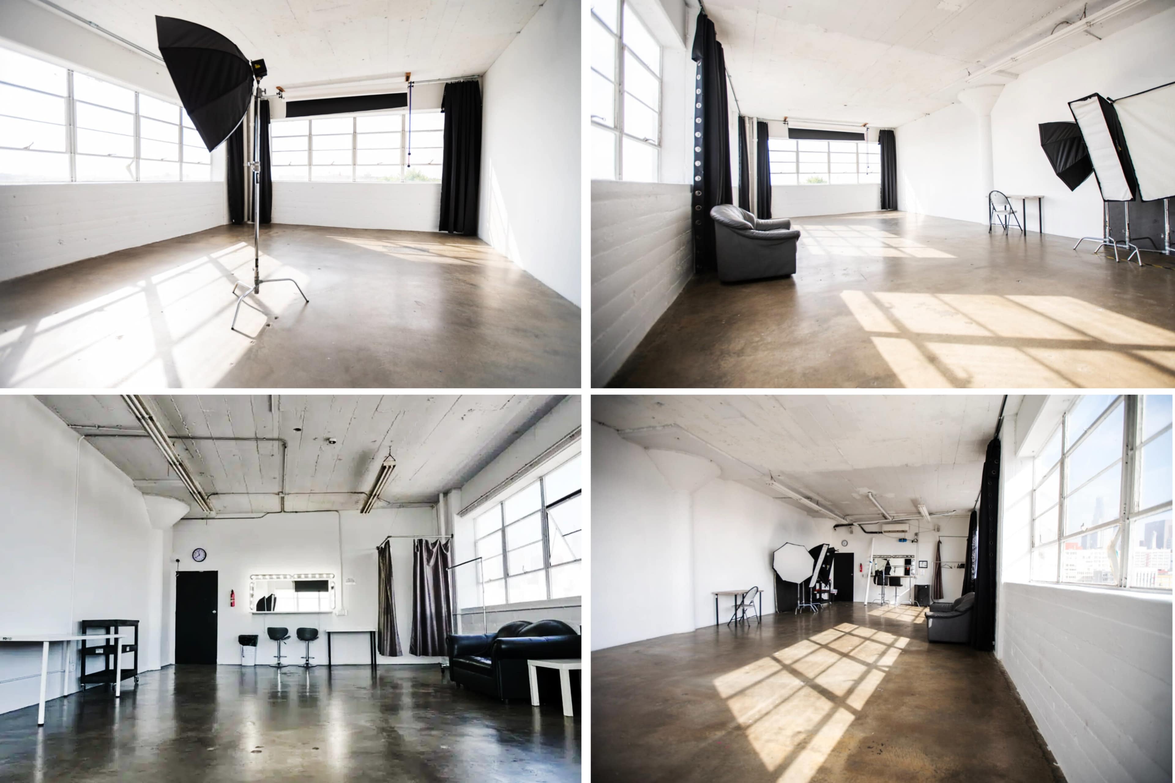 An empty photography studio with large windows, a concrete floor, and minimal furnishings, including a black sofa and several lighting setups.