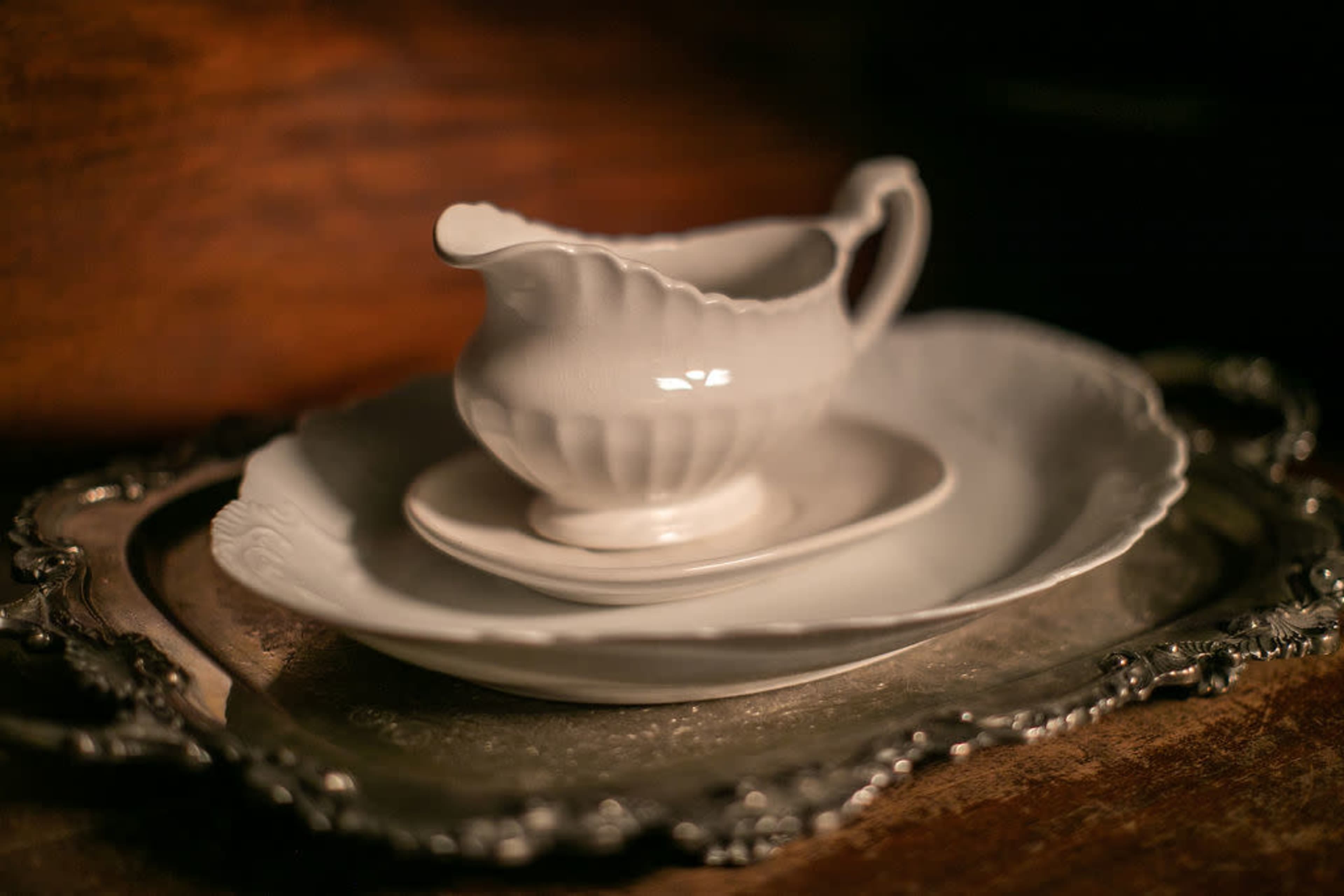 A white ceramic creamer sits atop a small plate, which is placed on a larger plate, all arranged on a silver tray.