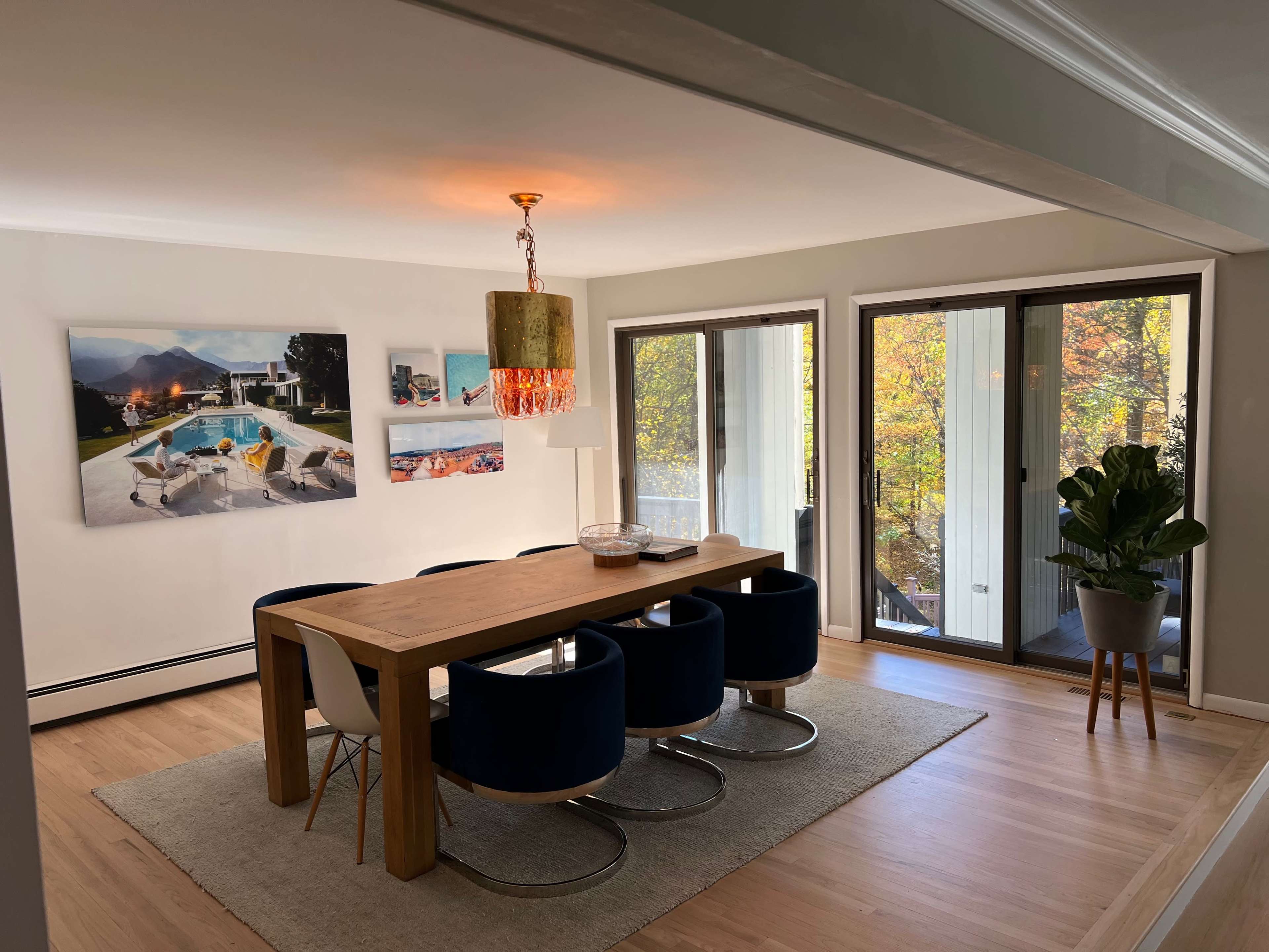 A spacious dining area features a wooden table surrounded by blue chairs, with large windows offering views of autumn foliage.