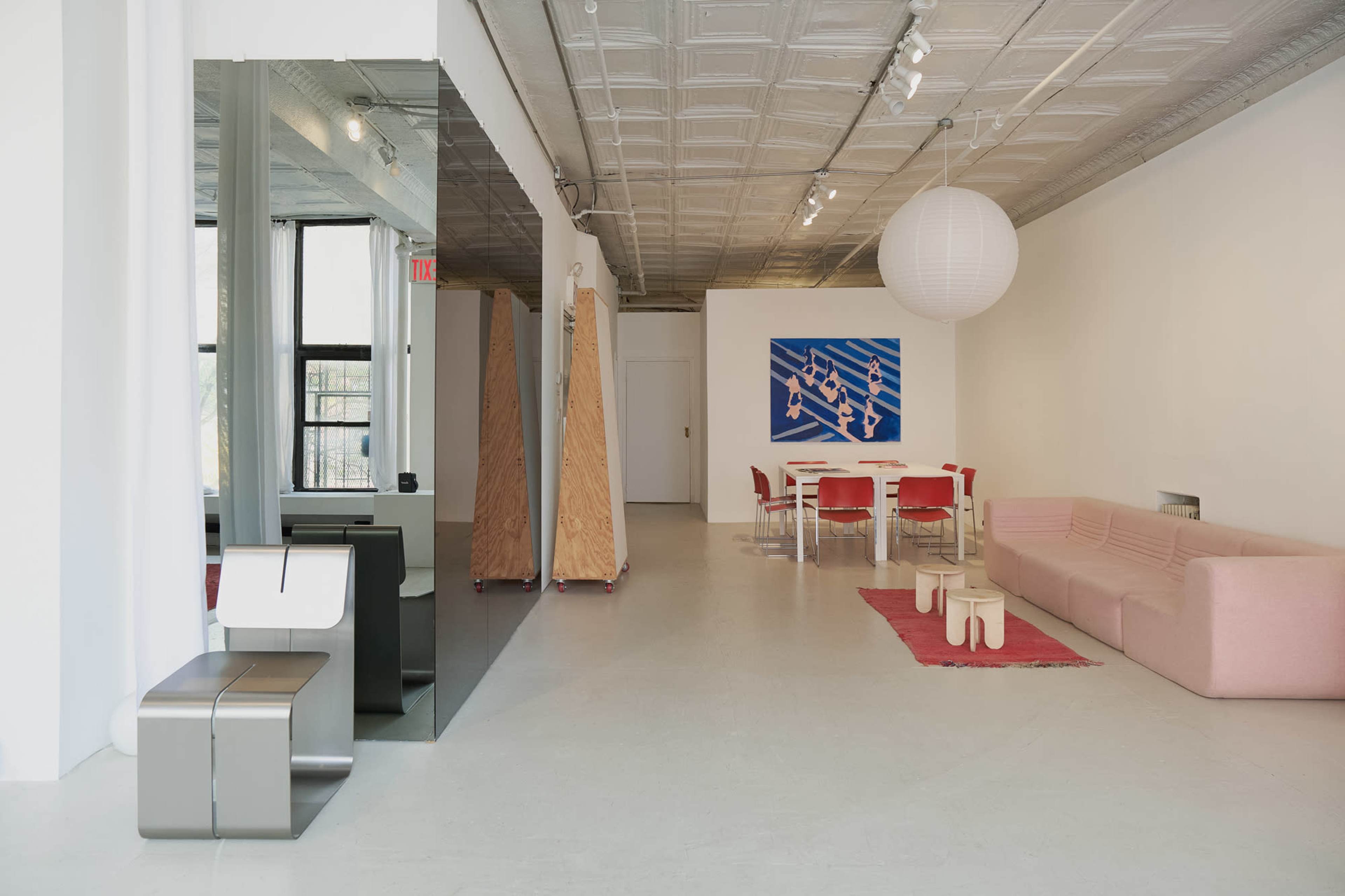 The image shows a modern interior space featuring a pink sofa, a white ceiling with light fixtures, a large mirror, and a dining table with red chairs.