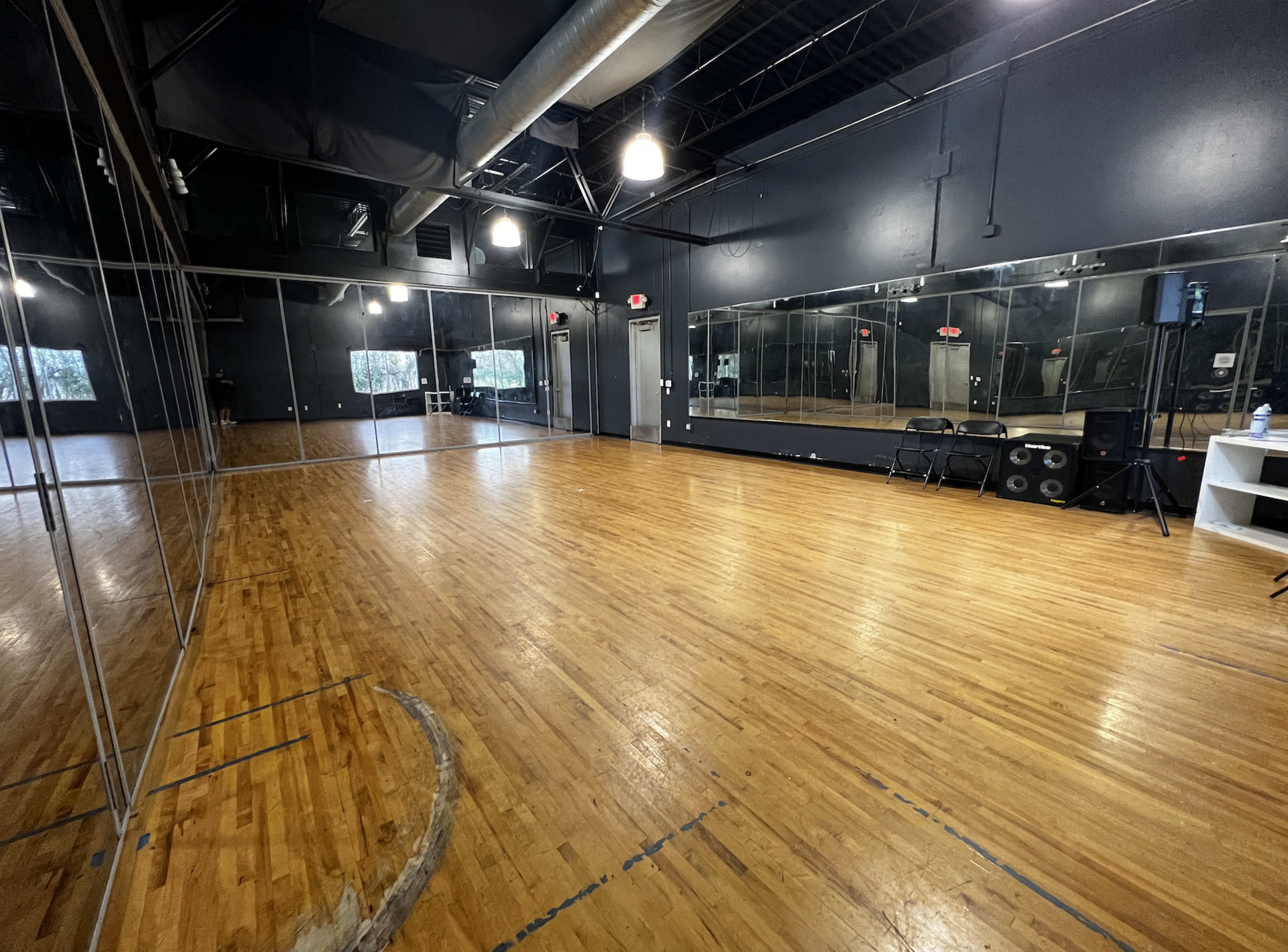 A spacious dance studio with wooden flooring, mirrored walls, and a microphone setup in one corner.