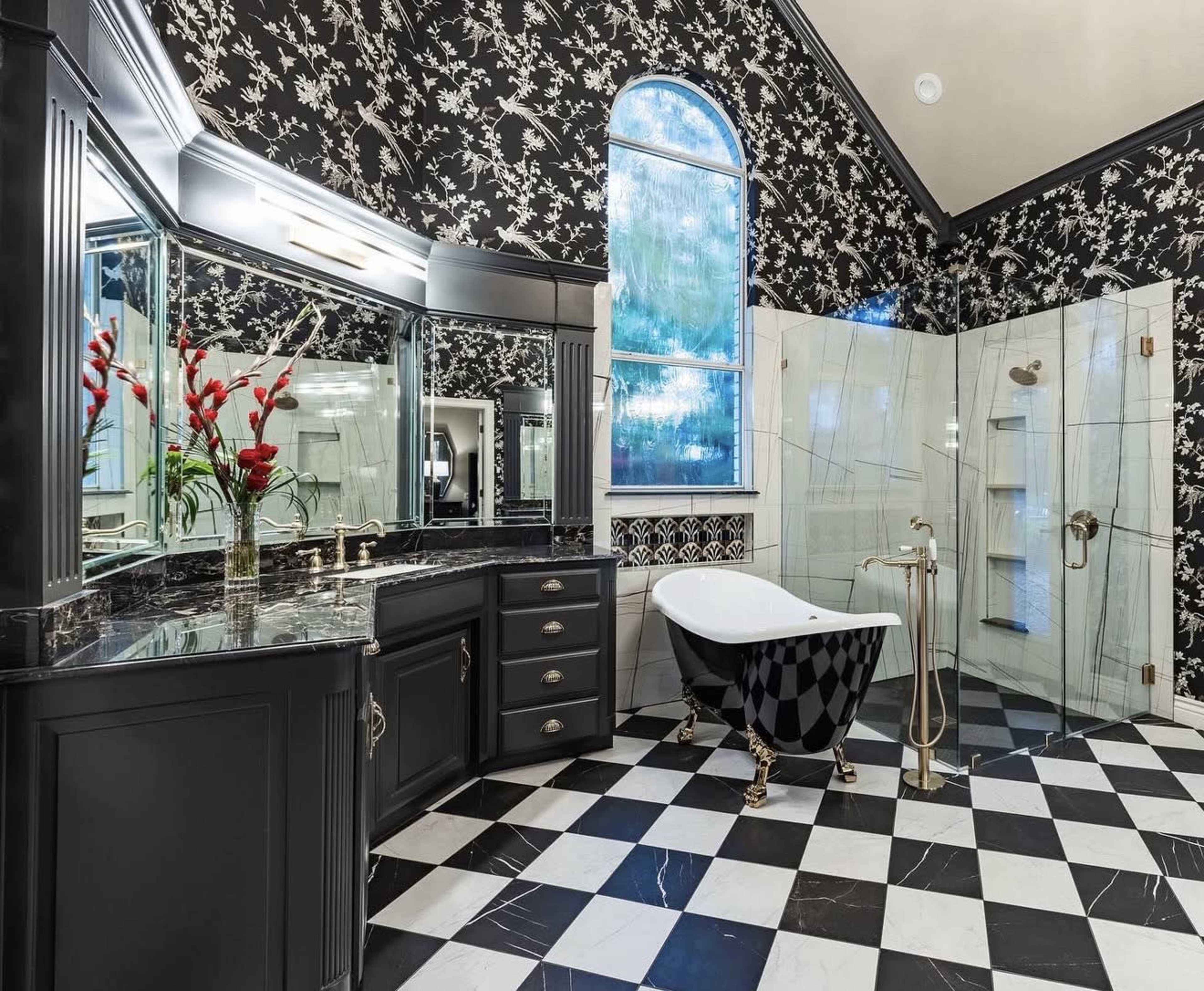 The bathroom features a black and white checkered floor, a freestanding bathtub, a glass-enclosed shower, and ornate floral wallpaper.