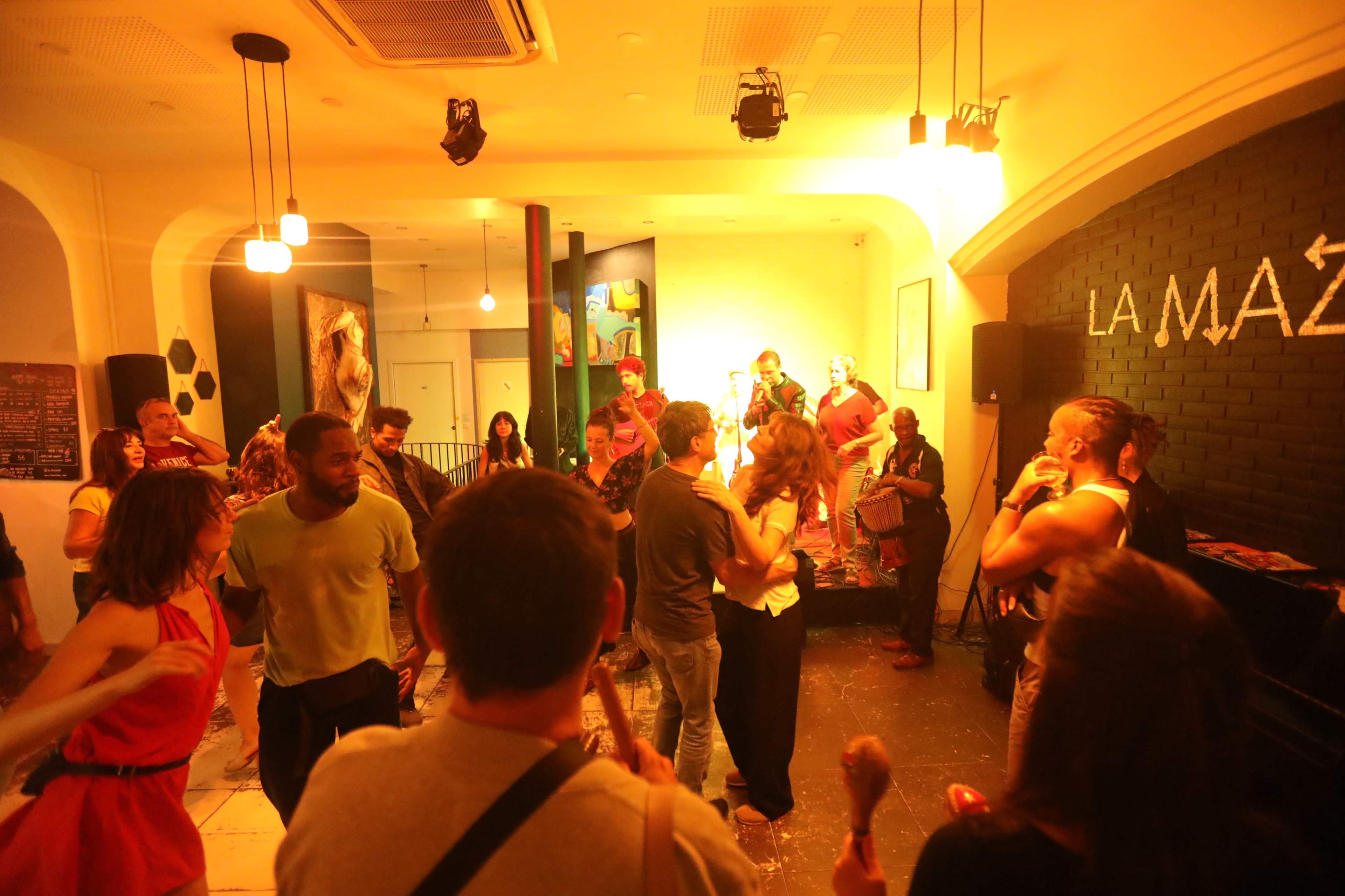 A lively gathering of people is dancing and enjoying music in a dimly lit venue adorned with colorful artwork.