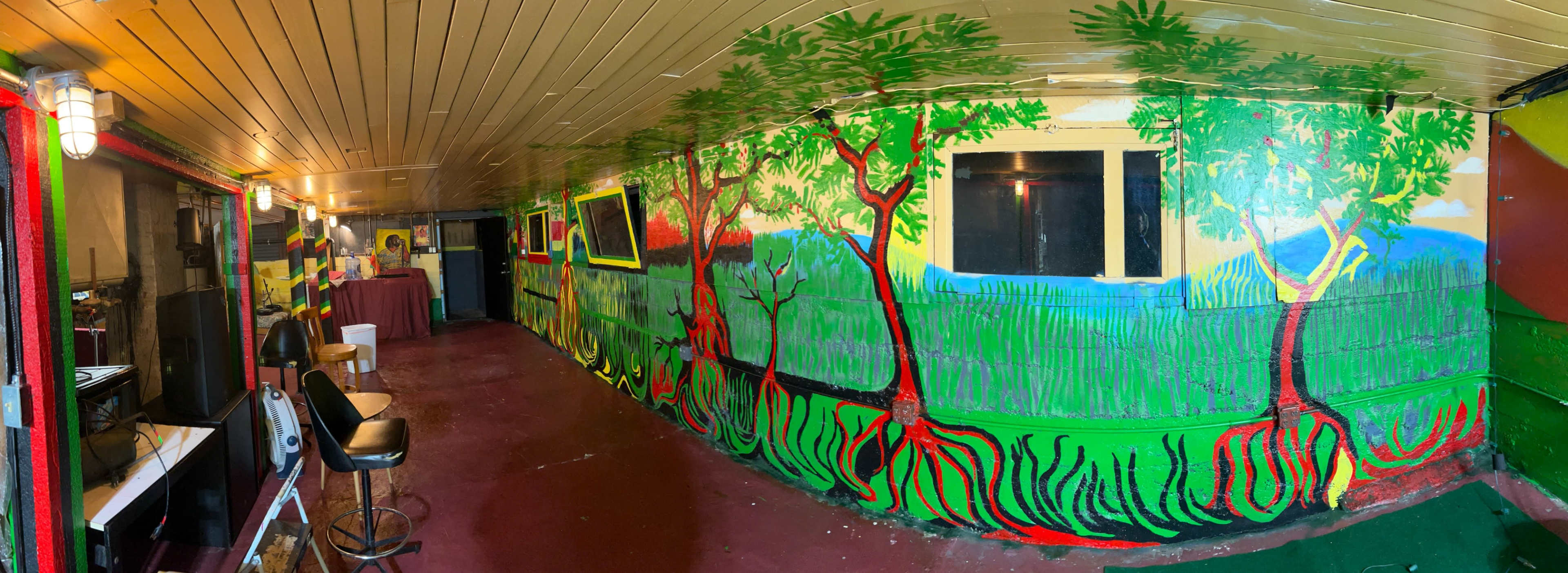 The image shows an indoor space featuring vibrant murals of trees on the walls, with a bar area and seating along one side.